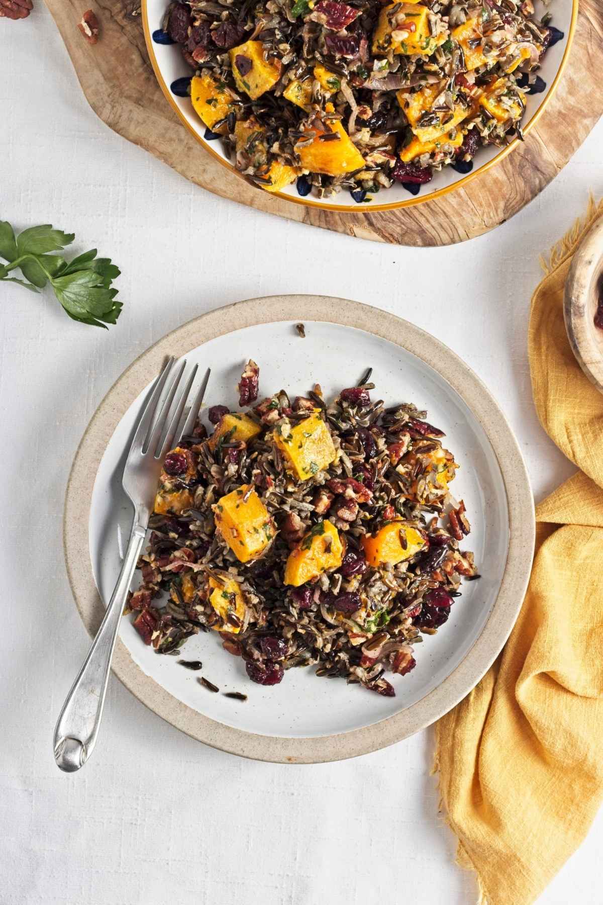 Wild rice salad with roasted butternut, cranberries, and pecans served on a ceramic plate.