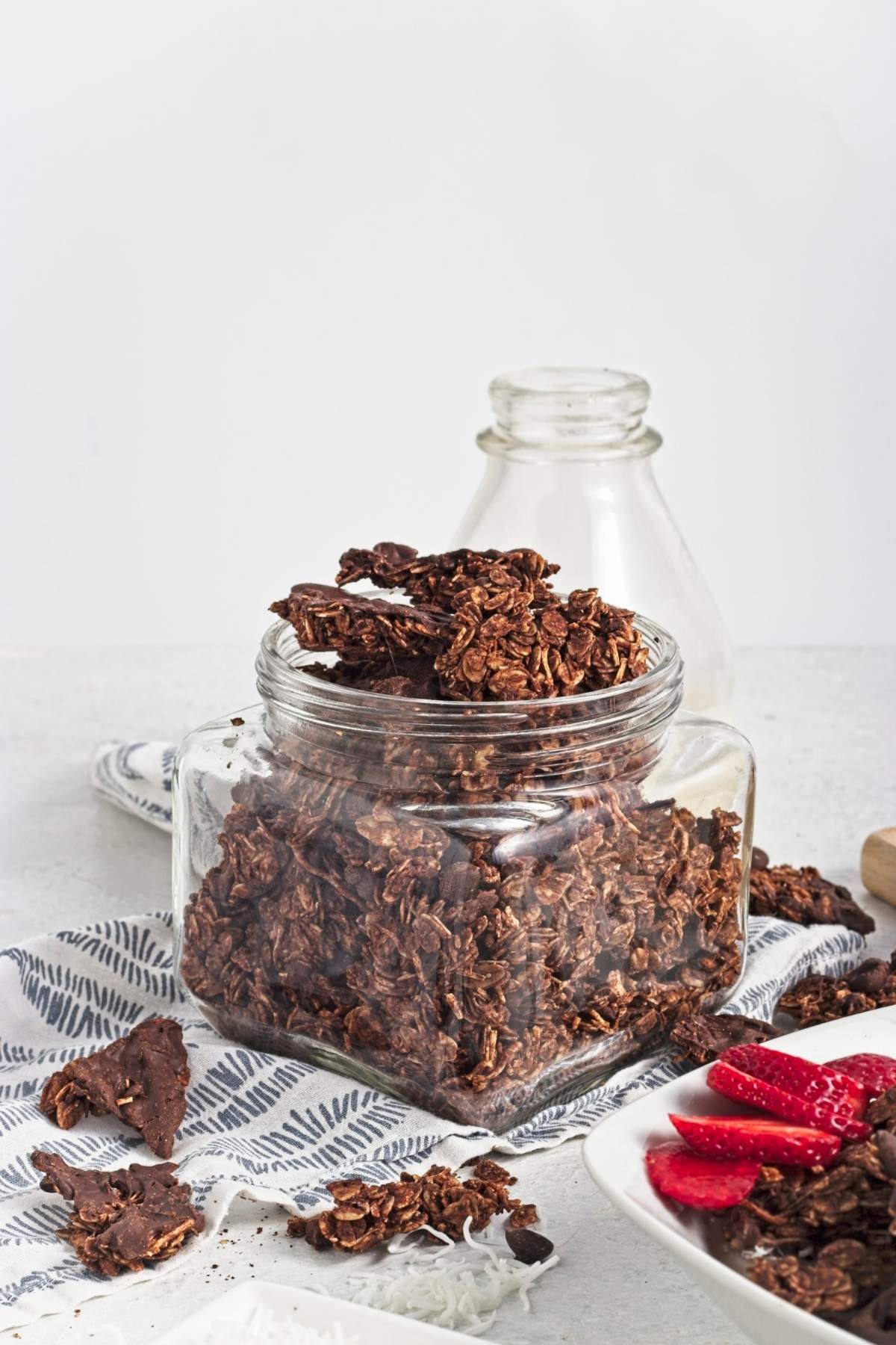 Glass jar filled with chunky chocolate granola clusters on a patterned cloth.