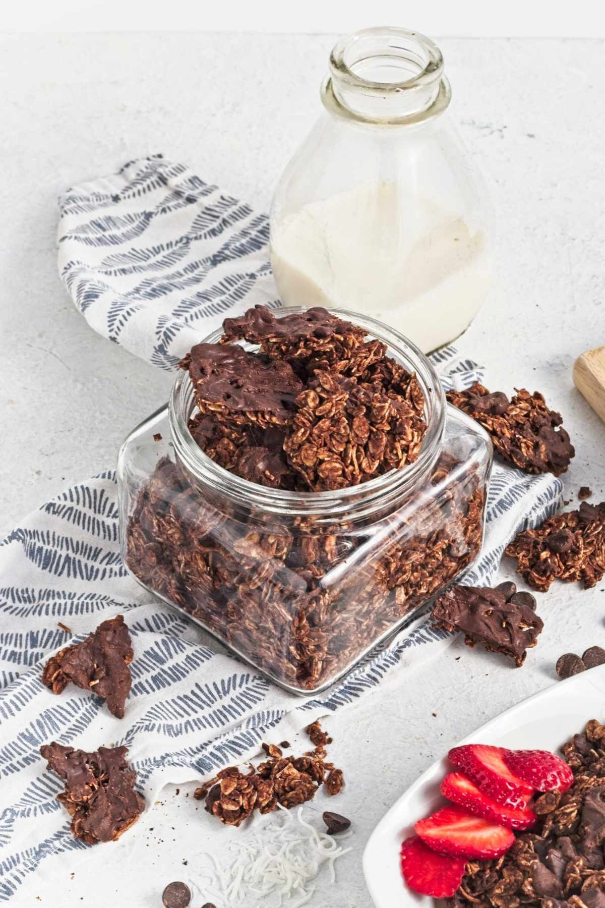 Chocolate granola clusters stored in a glass jar with broken pieces scattered around.