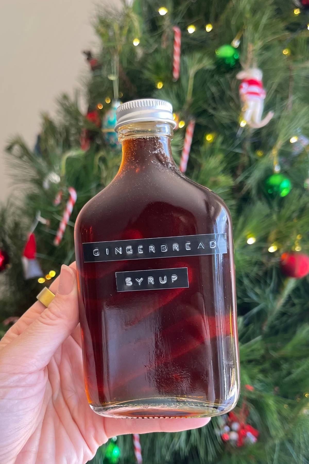 Glass bottle of gingerbread syrup held in front of a decorated tree.