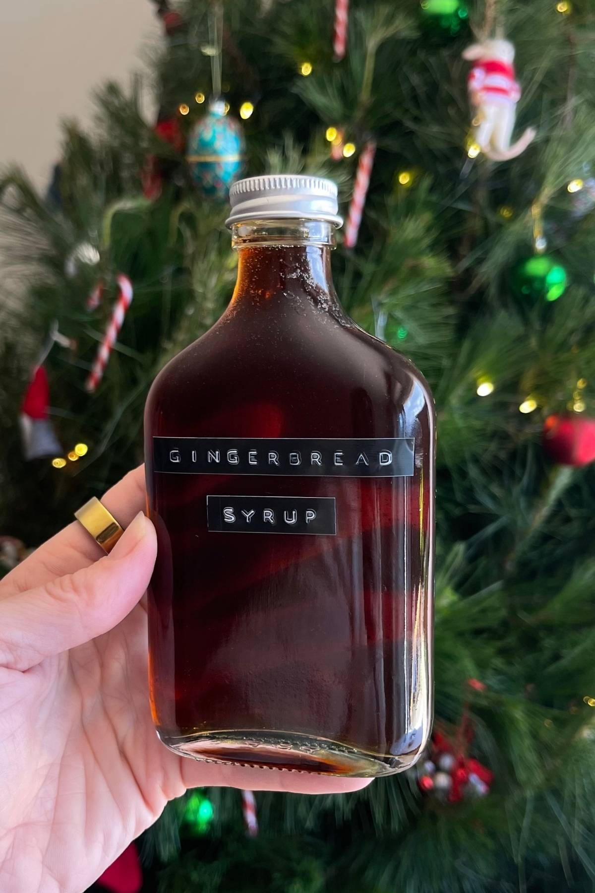 Hand holding a sealed glass bottle of dark syrup.