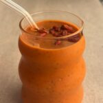 Creamy orange smoothie in a glass, topped with soaked goji berries on the surface.