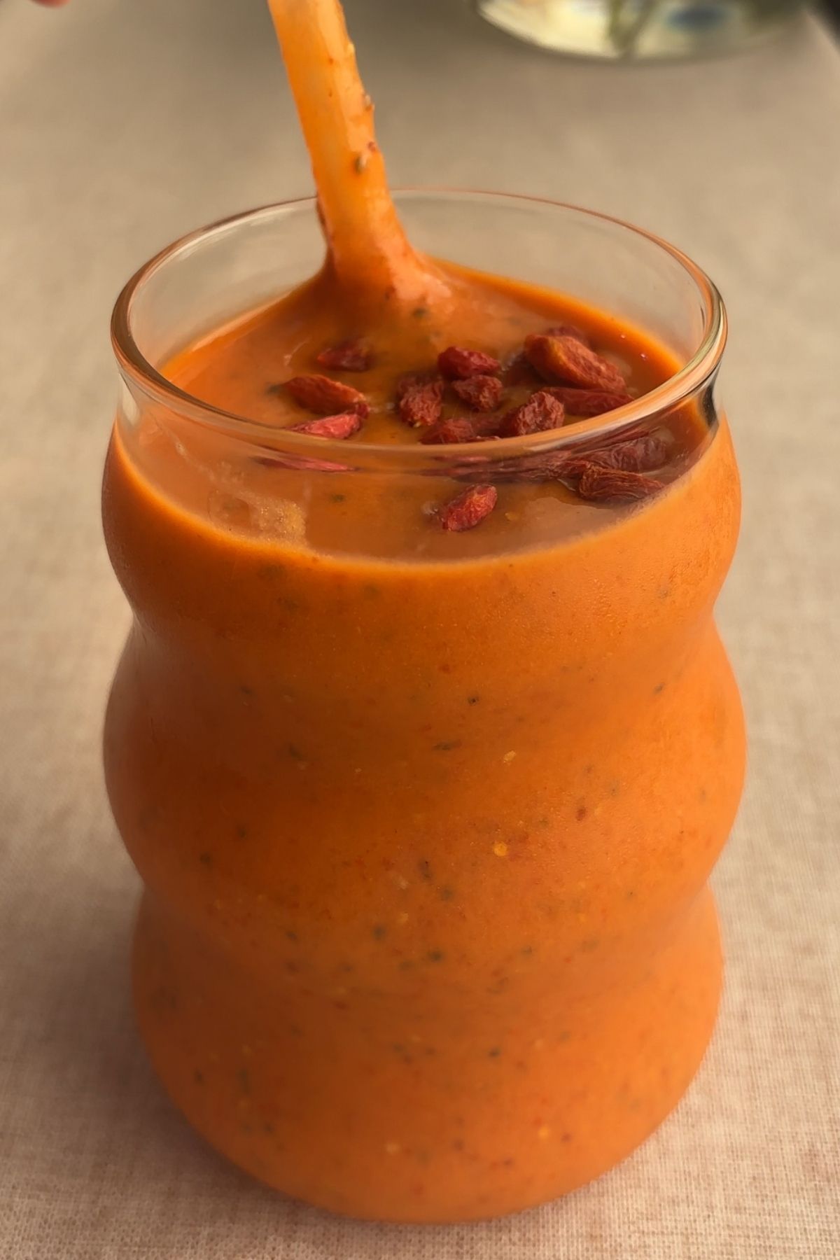 Thick orange smoothie being poured into a glass, topped with soaked goji berries.