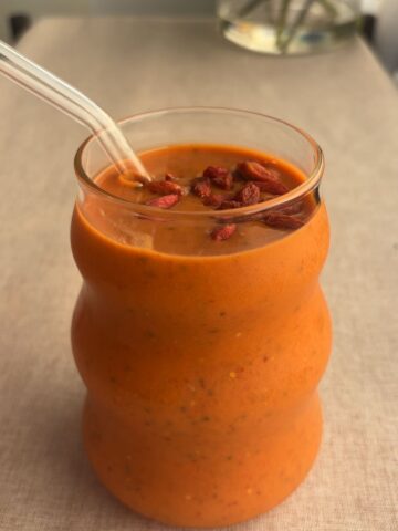 Creamy orange smoothie in a glass, topped with soaked goji berries on the surface.
