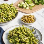 Green goddess pasta salad served on a plate with herbs, olives, and cucumber.