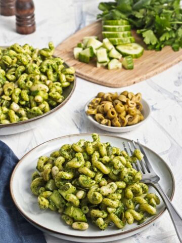 Green goddess pasta salad served on a plate with herbs, olives, and cucumber.