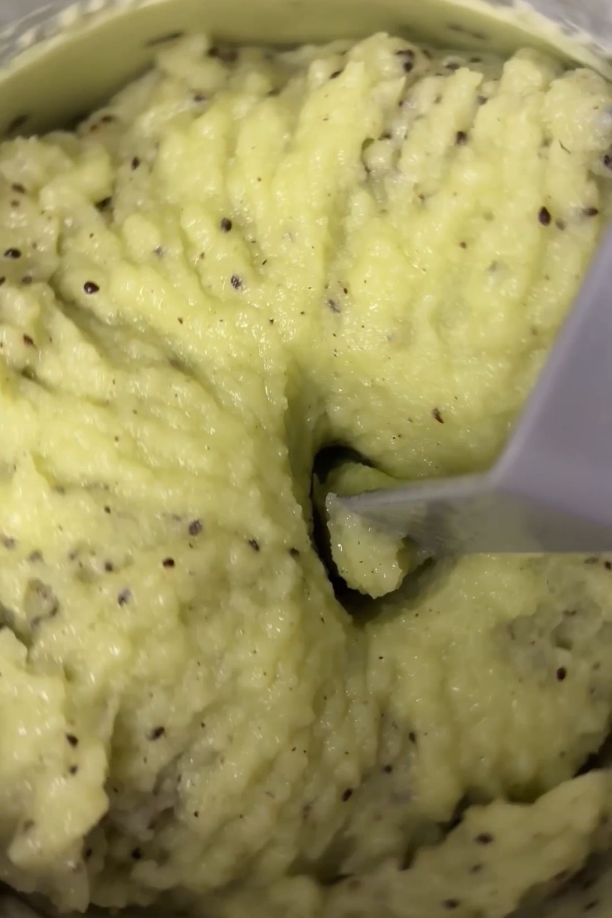 Kiwi sorbet mixture being scooped from a freezer-safe container, showing a thick, icy texture with visible kiwi seeds.