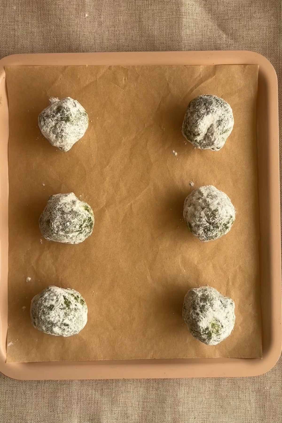 Sugar coated matcha cookie dough arranged on a lined baking tray.