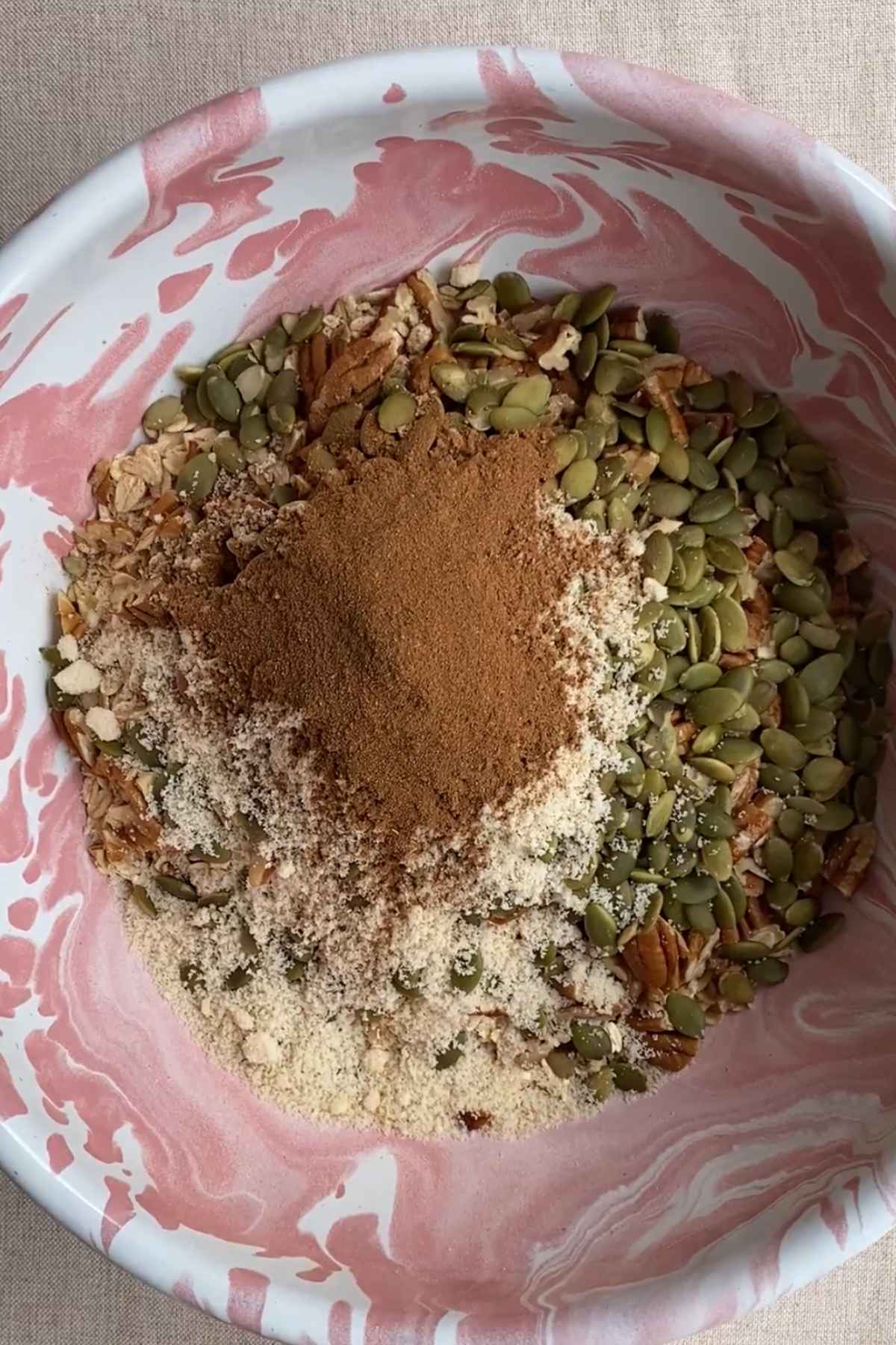 Rolled oats, pecans, pepitas, almond meal, and spices combined in a mixing bowl.