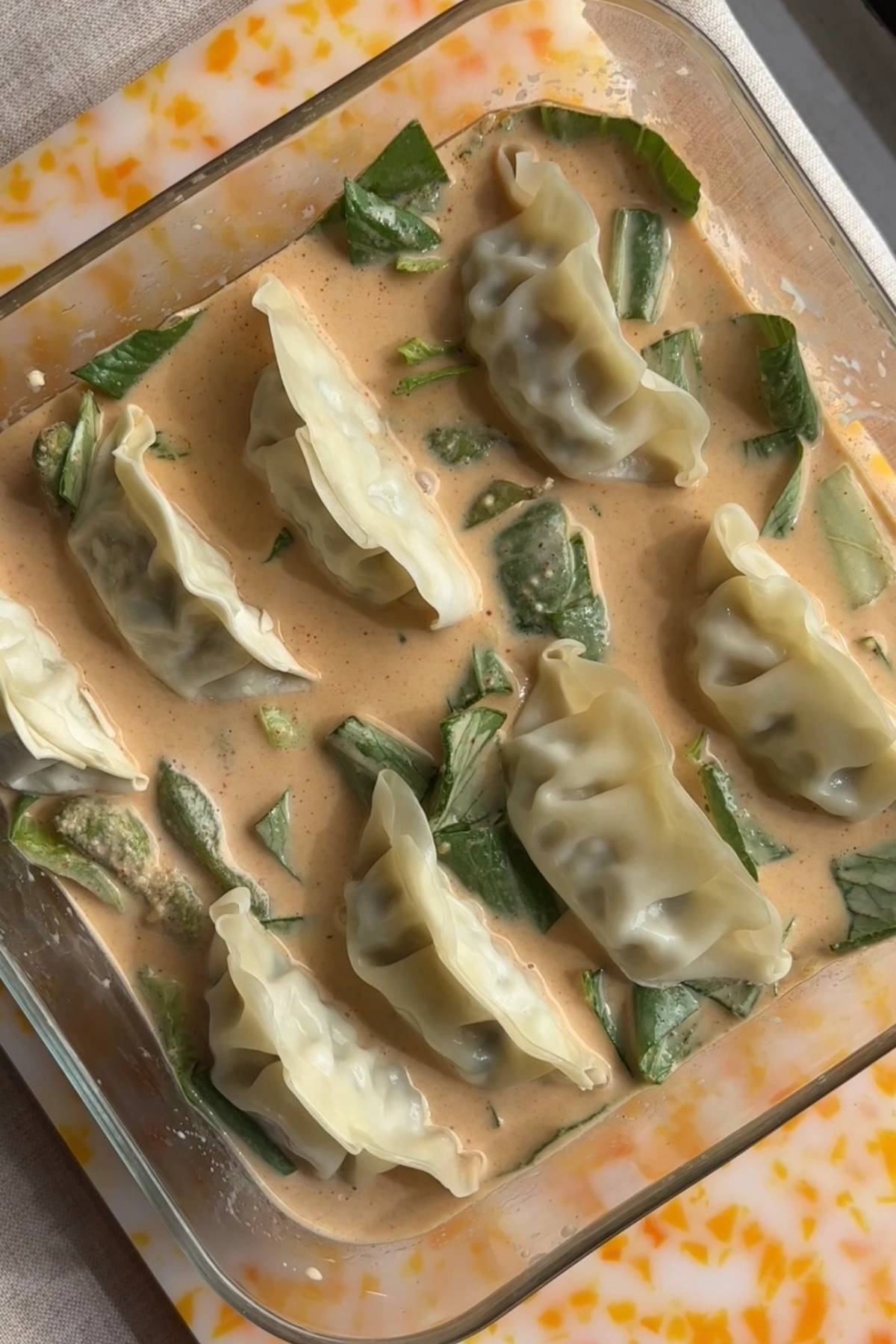Frozen dumplings nestled into the curry sauce with bok choy and edamame before baking.
