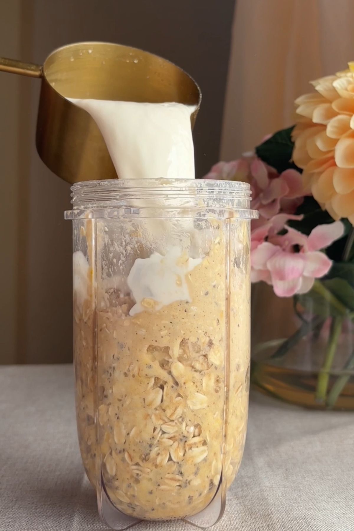 Milk being poured into a blender cup filled with chunky oat batter.
