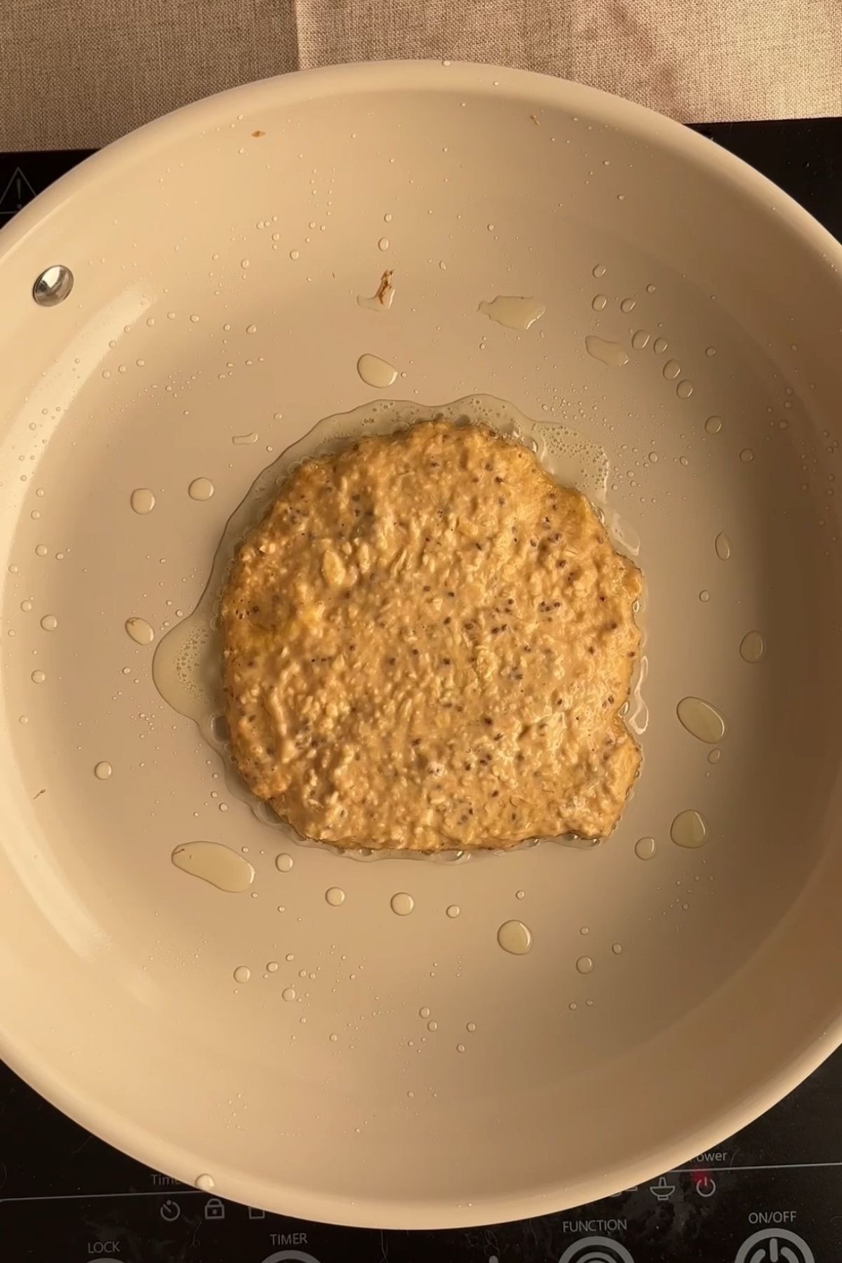 A raw pancake batter round cooking in an oiled pan.