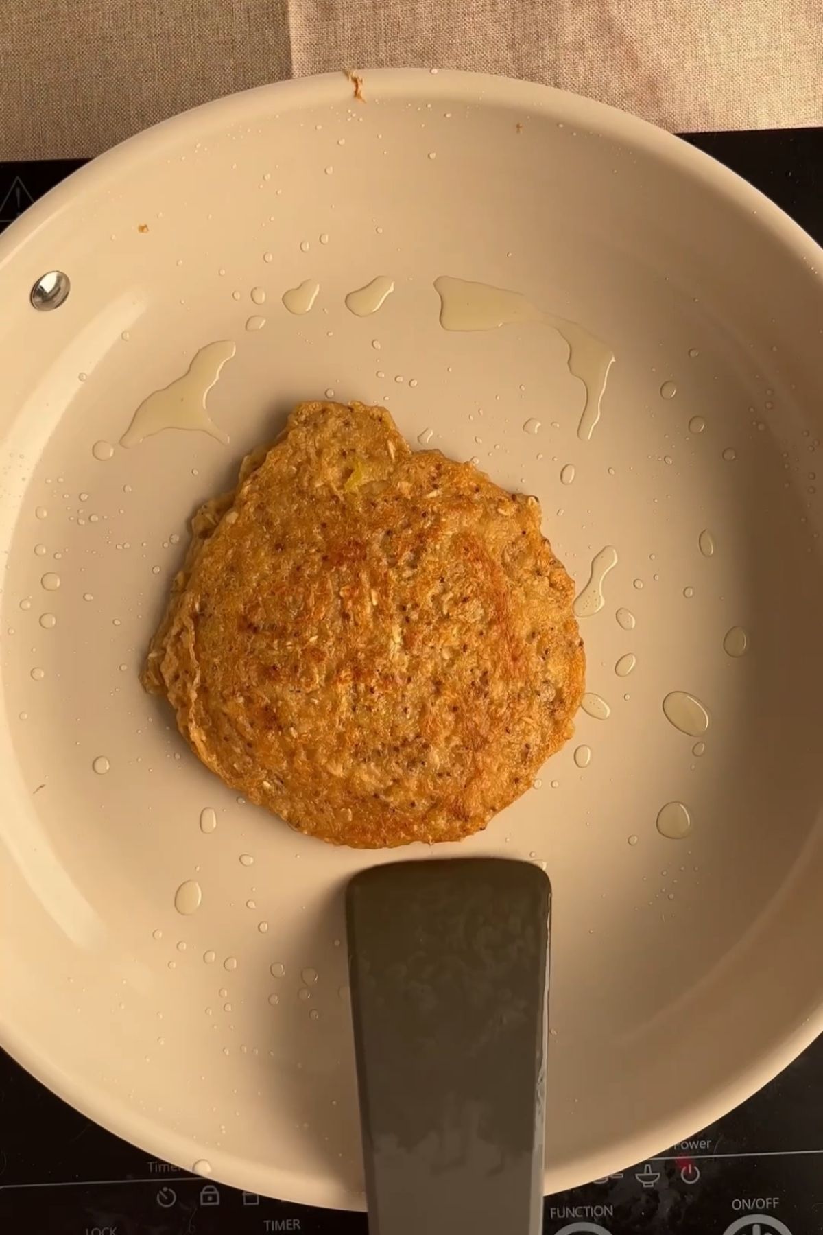 A golden pancake cooking in an oiled pan.
