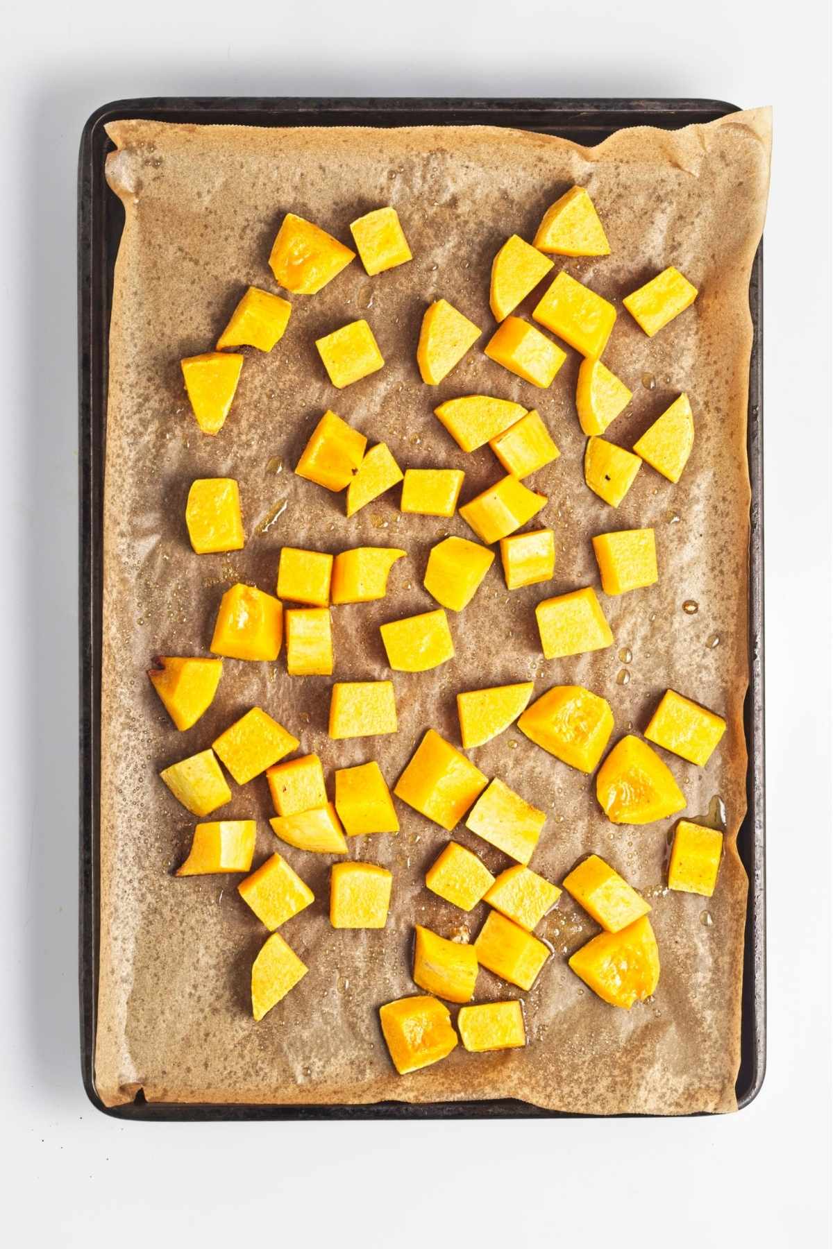 Roasted butternut squash cubes spread on a parchment-lined baking tray.
