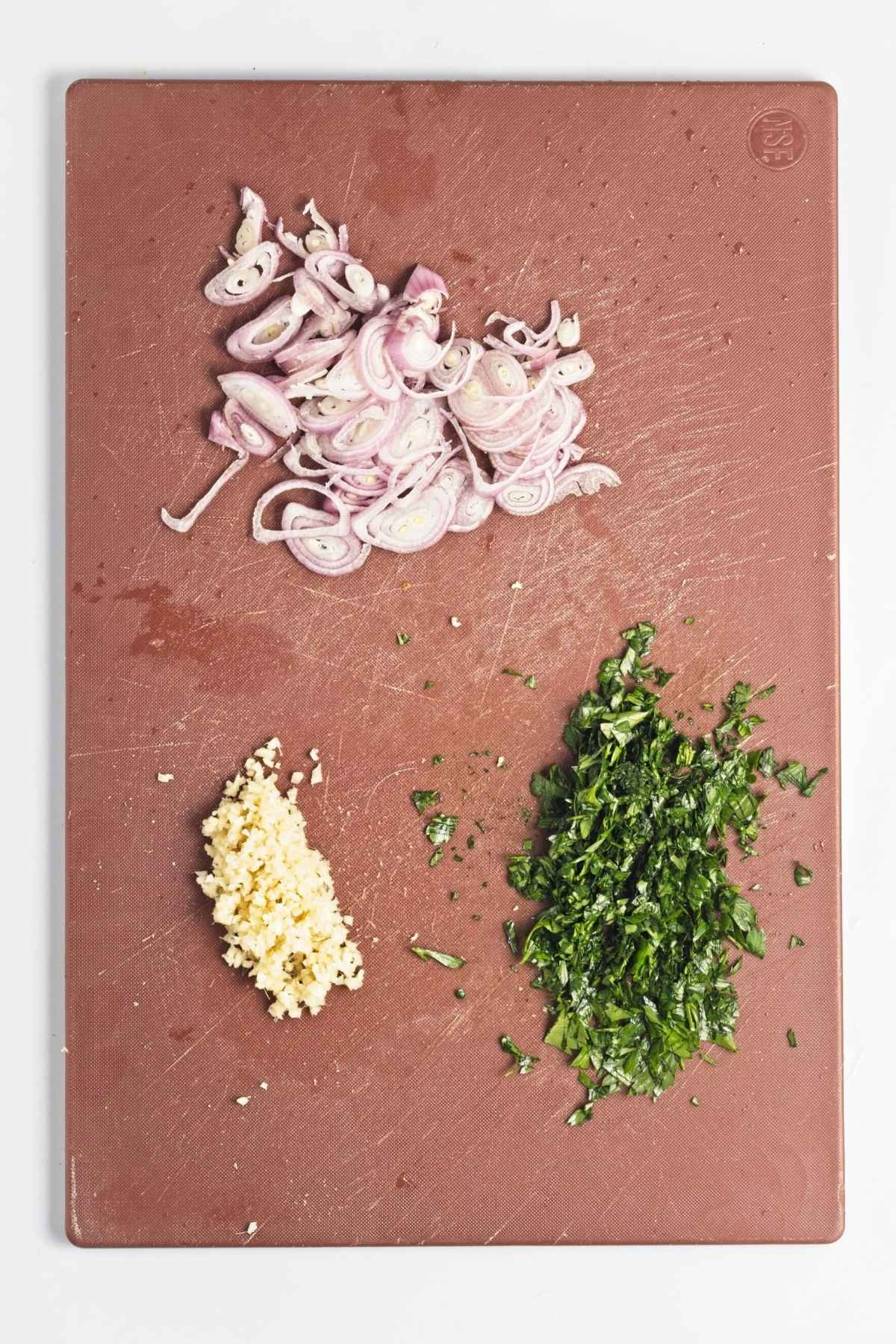 Sliced shallots, minced ginger, and chopped parsley on a cutting board.