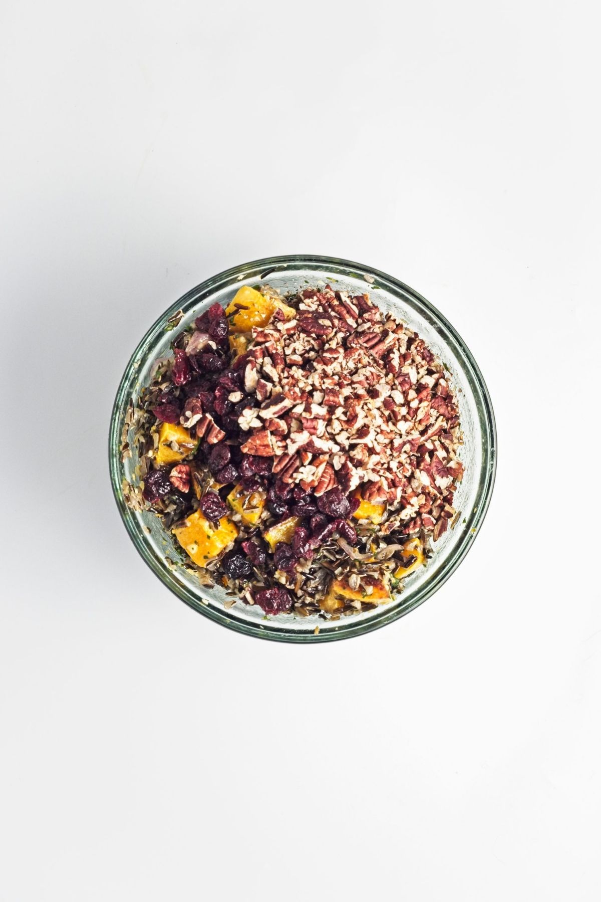 Finished wild rice salad in a glass bowl topped with chopped pecans and dried cranberries.
