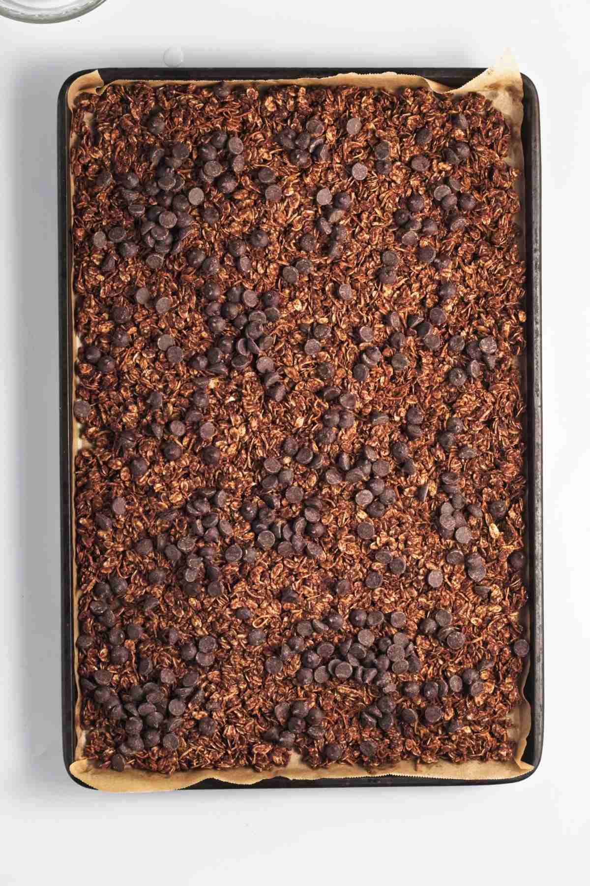 Melted chocolate swirled over baked chocolate granola on a tray.