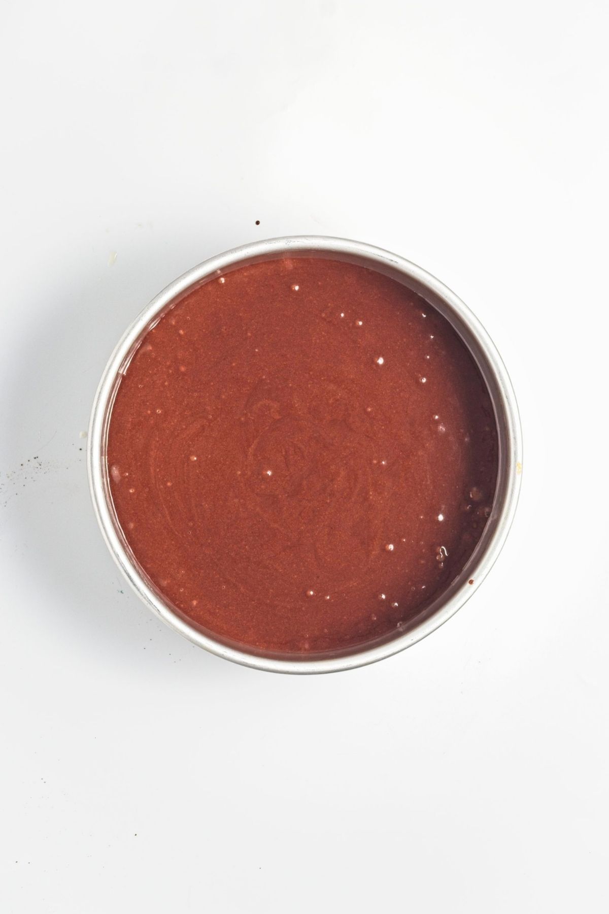 Smooth chocolate cake batter evenly spread in a round baking pan.