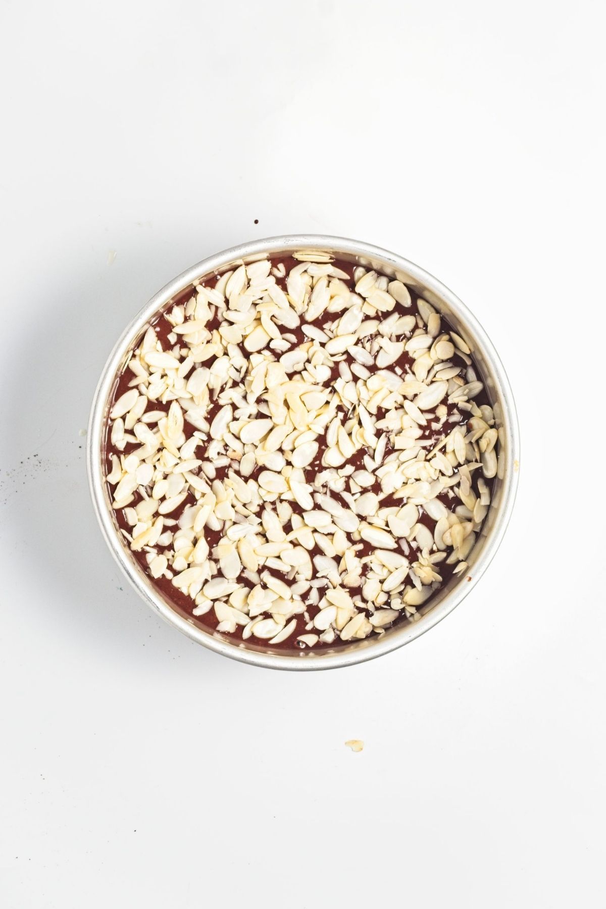 Cake batter poured into a round baking pan and topped with sliced almonds.