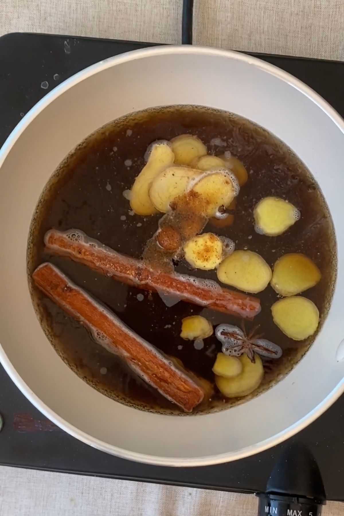Water and brown sugar simmering with sliced ginger and whole spices in a saucepan.