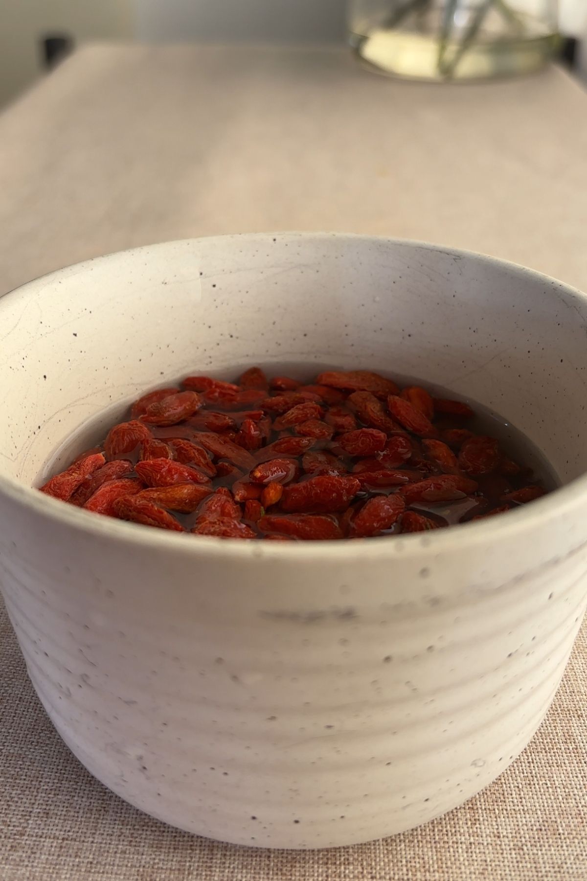 Dried goji berries soaking in water inside a white bowl.