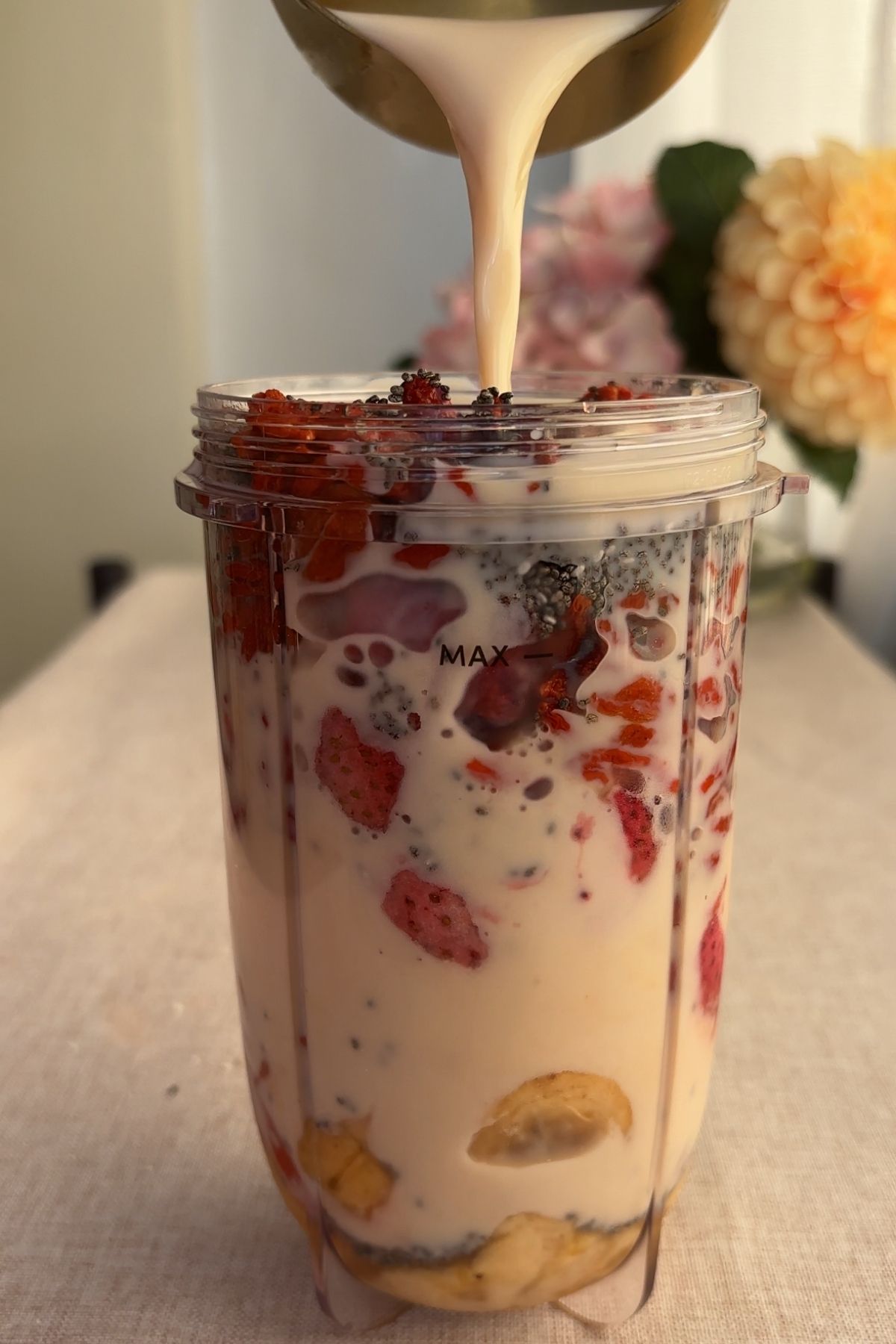 Banana slices, strawberries, chia seeds, and milk layered in a blender cup.