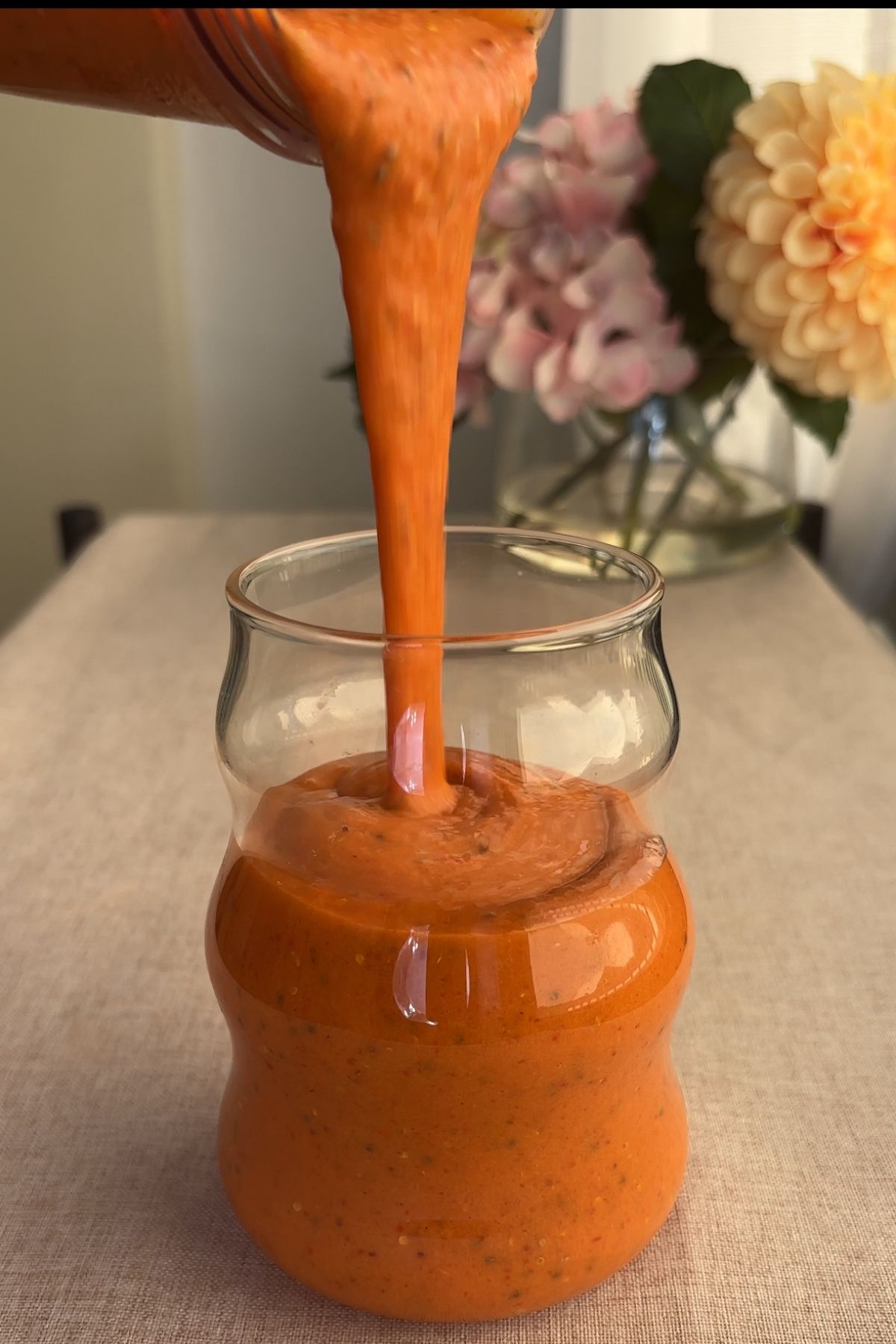 Thick orange smoothie being poured from a blender into a glass.