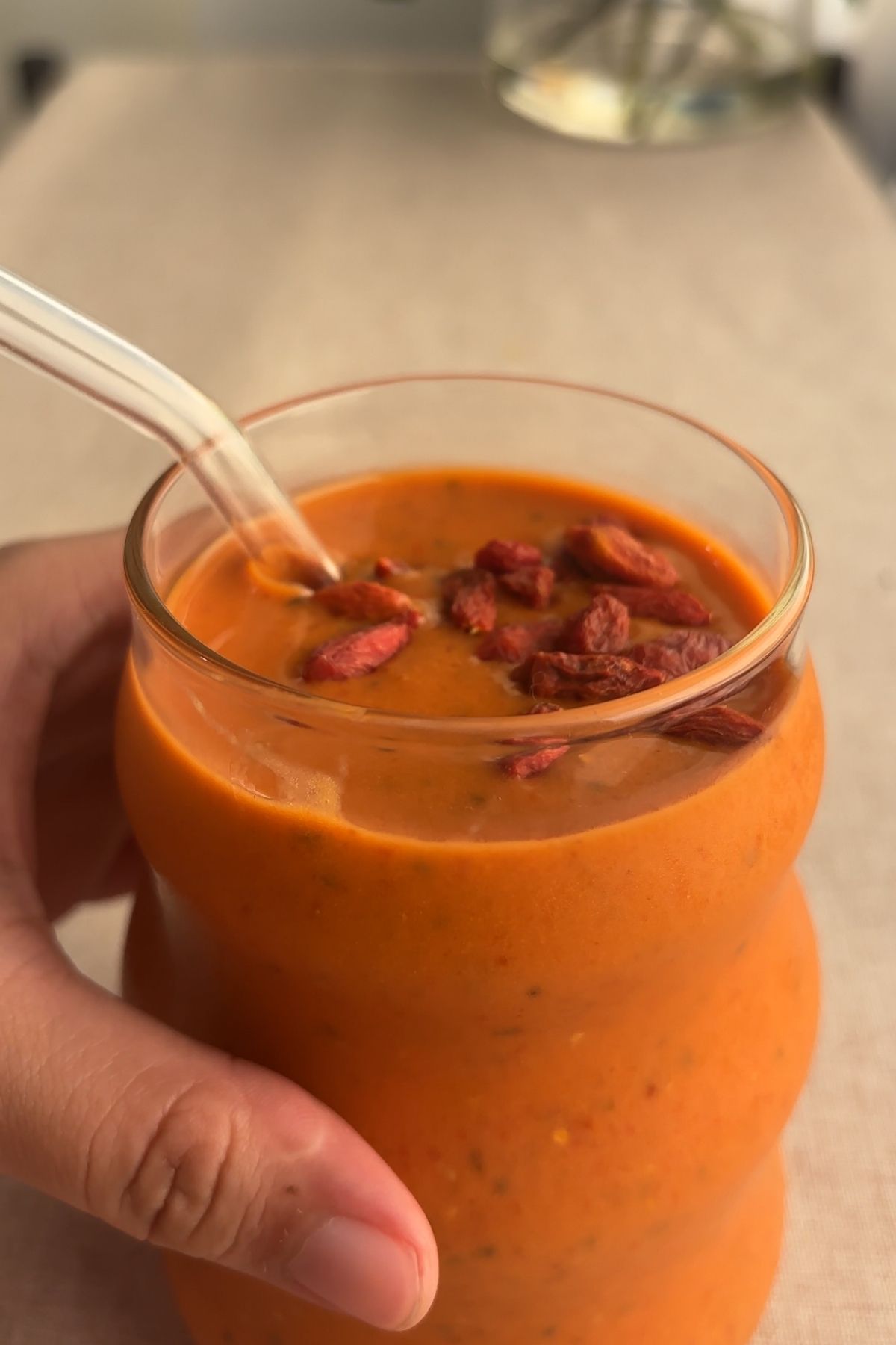 Hand holding a glass of orange smoothie topped with soaked goji berries.