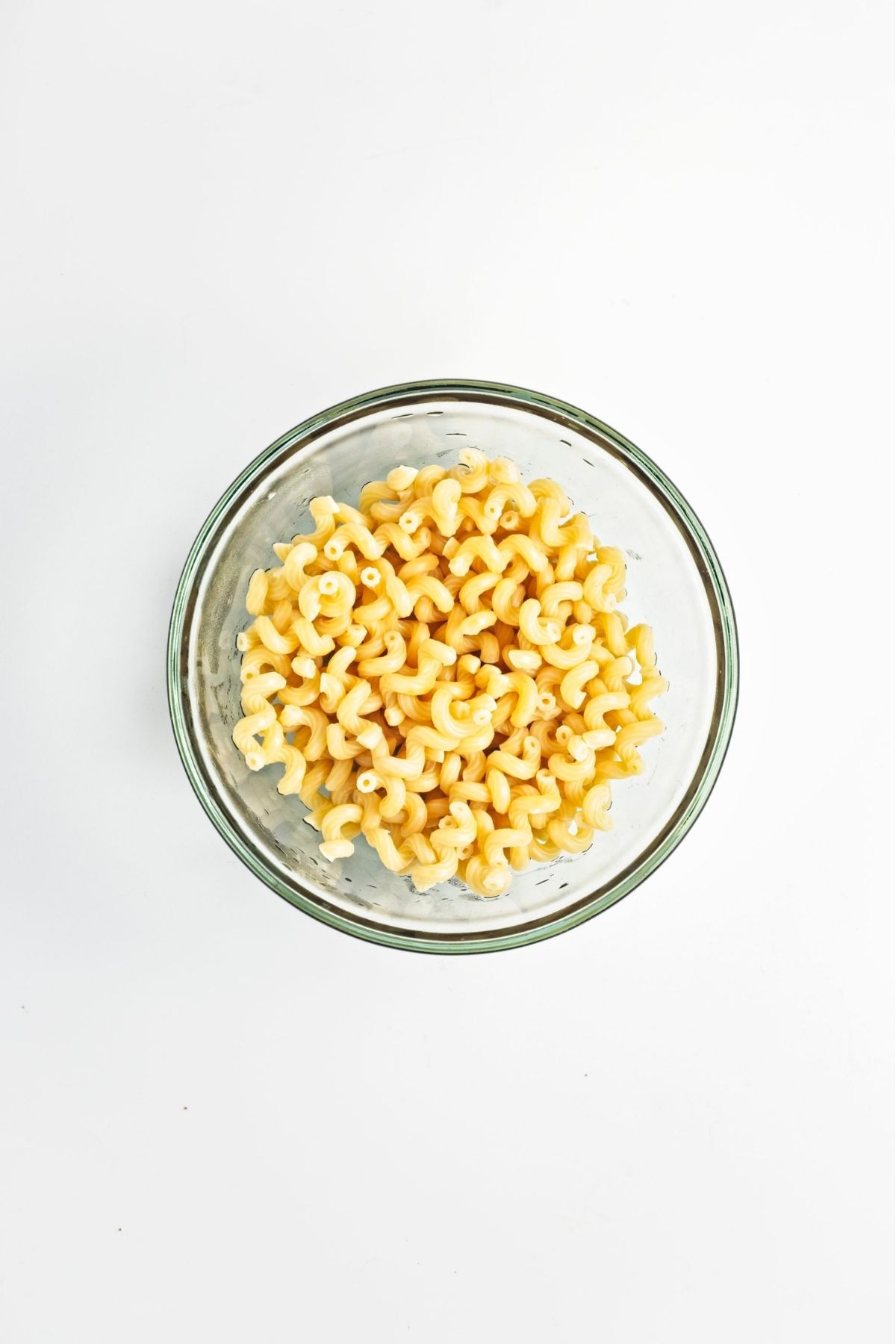Cooked short pasta cooling in a clear glass bowl on a white surface.