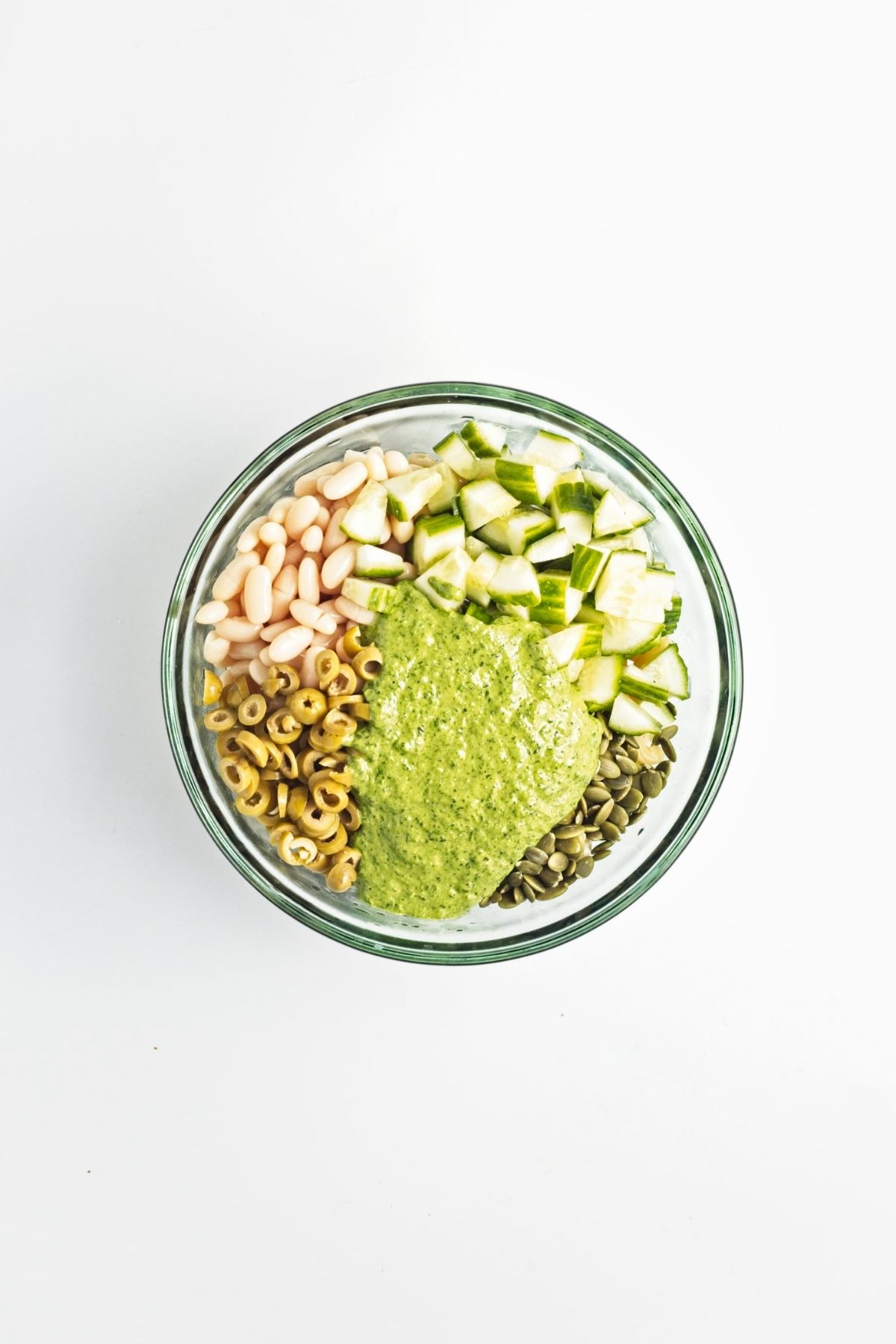 Green herb dressing poured over pasta mixture in a large bowl.