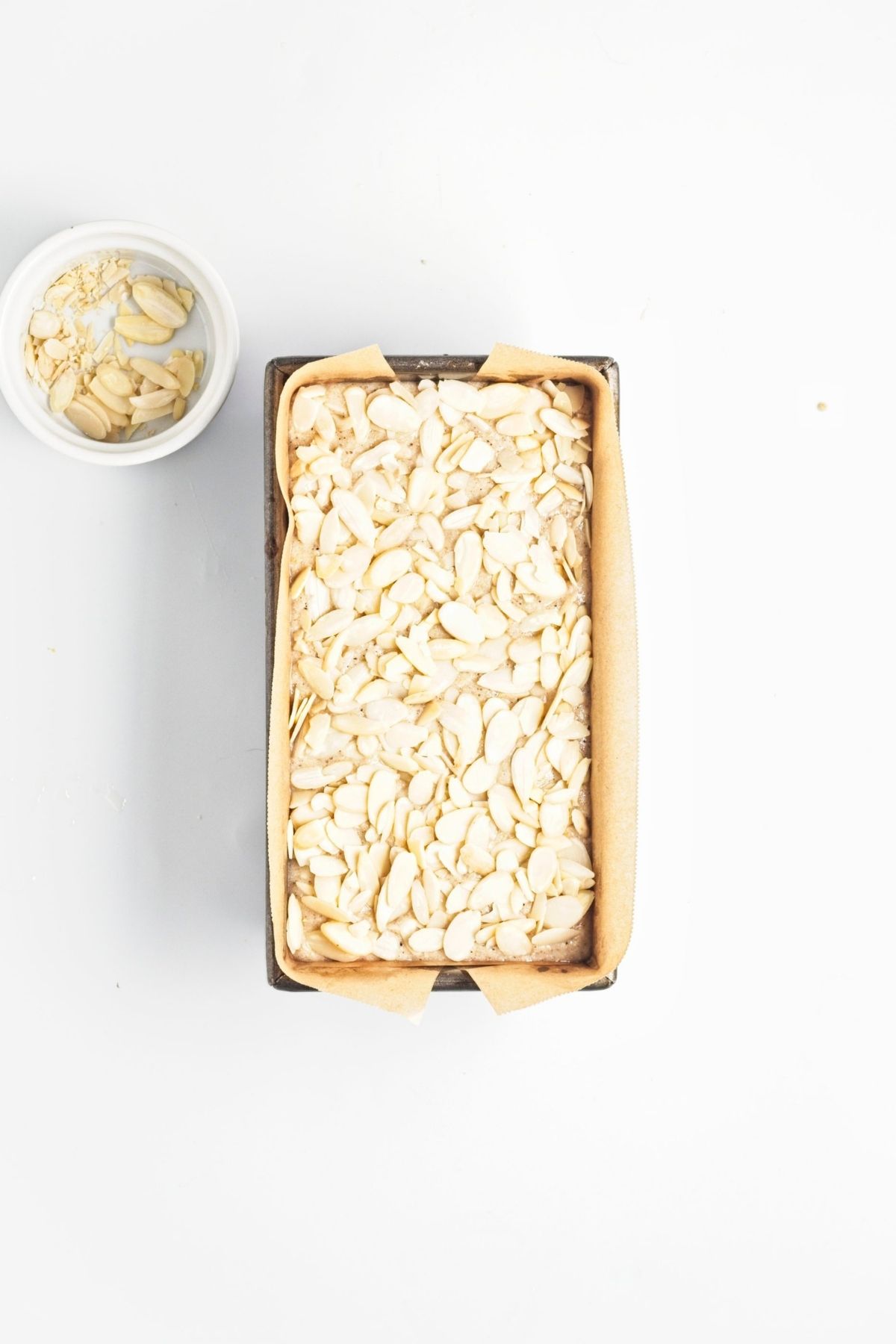 Lemon almond loaf batter spread into a lined loaf pan and topped with almonds.