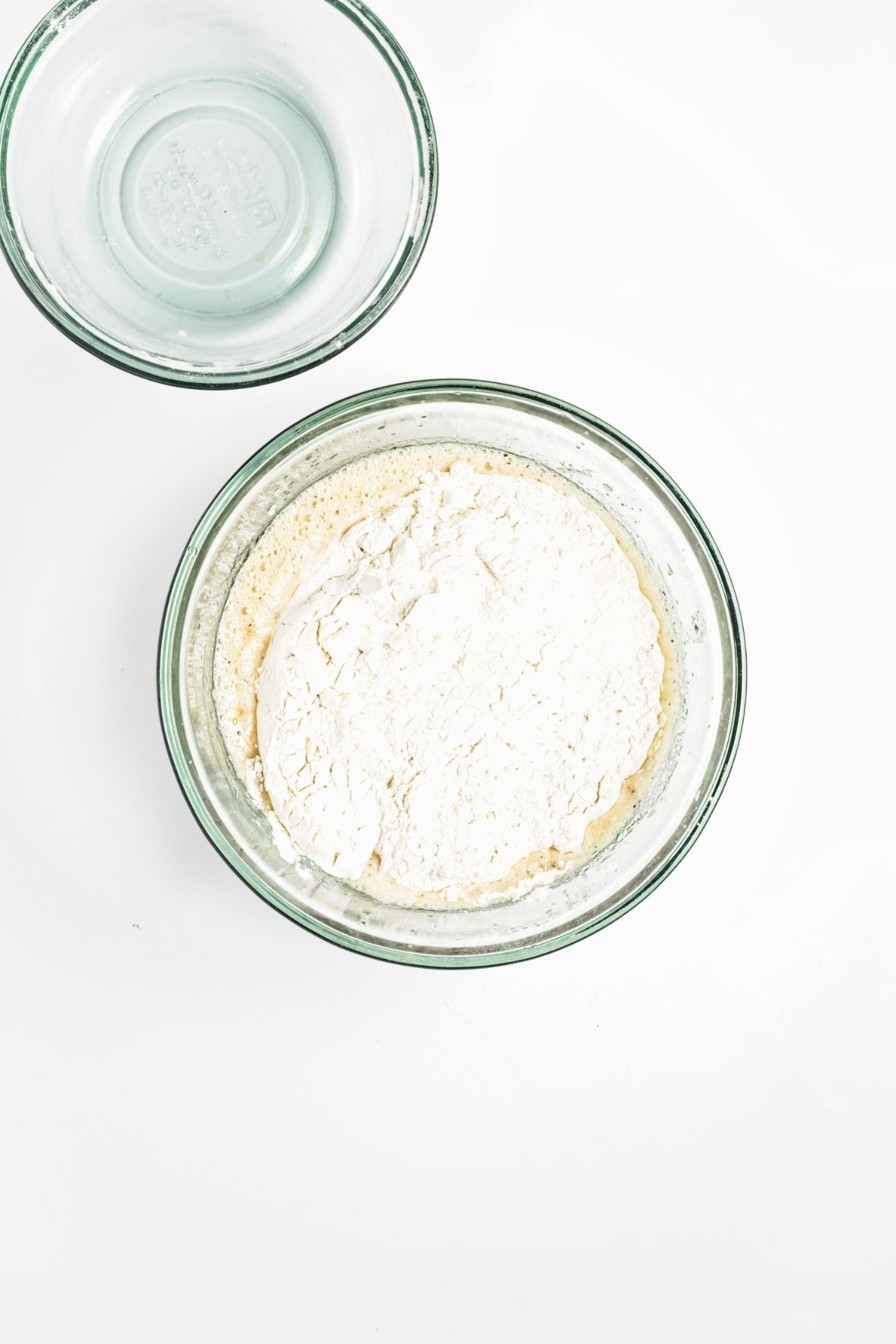 Flour mixture added to the wet batter in a glass mixing bowl.
