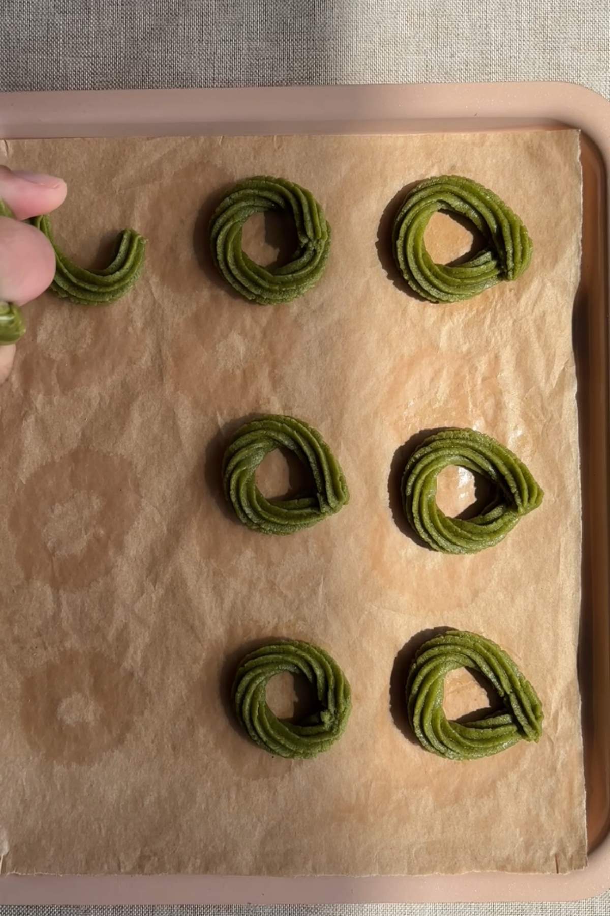 Piping matcha cookie dough into wreath shapes on parchment paper.