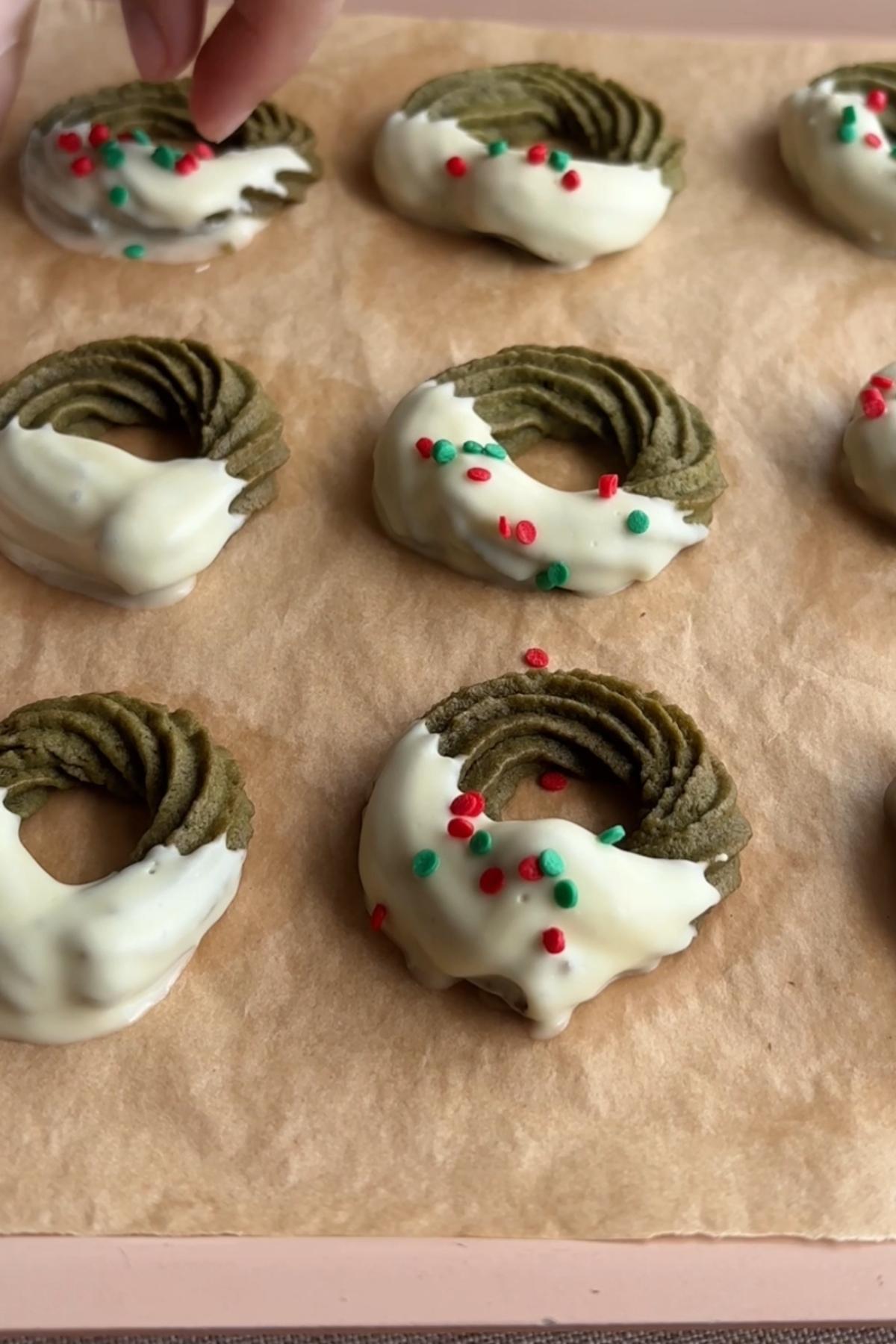 Sprinkling red and green decorations onto white chocolate coated cookies.