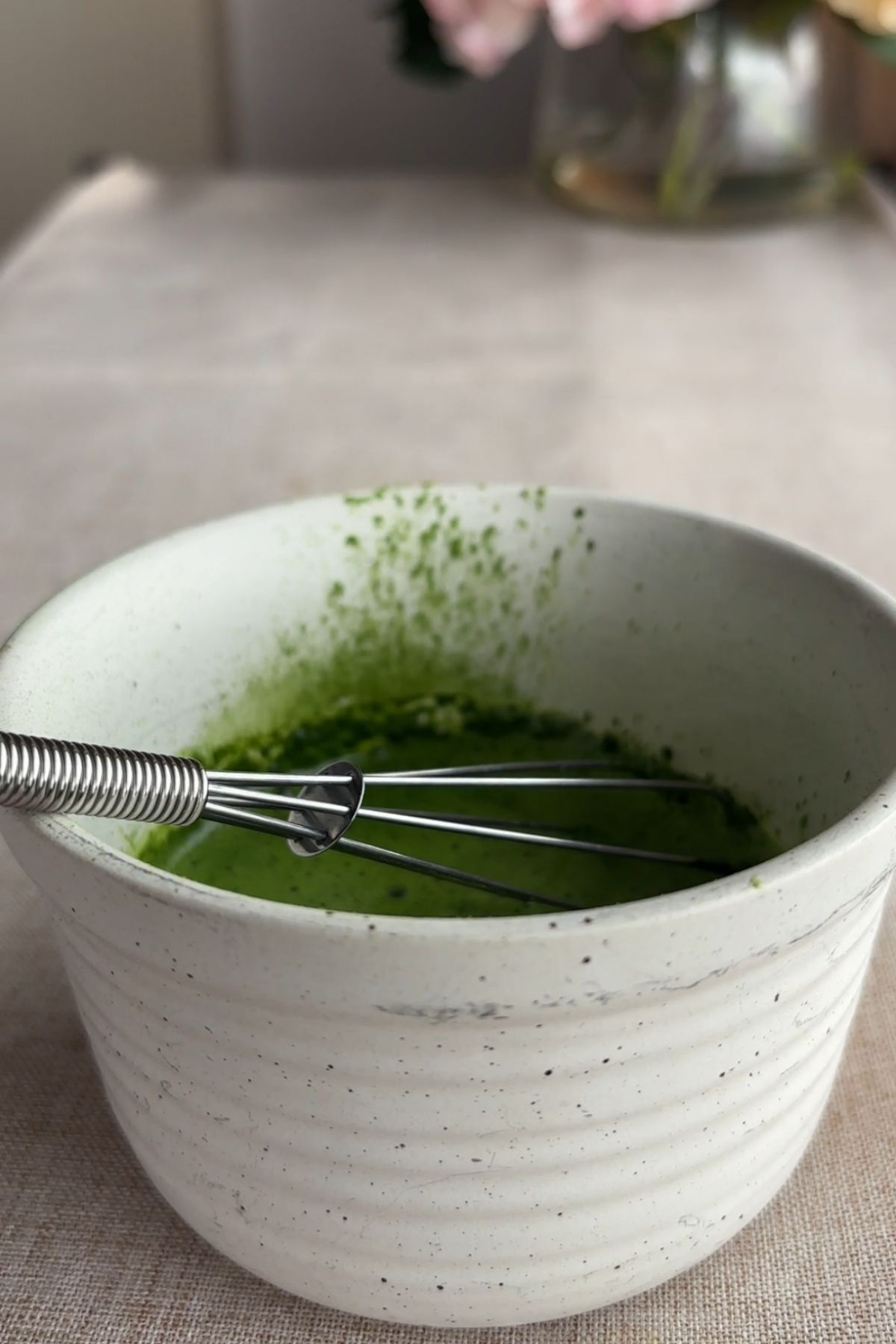 Matcha powder whisked with liquid in a small bowl.