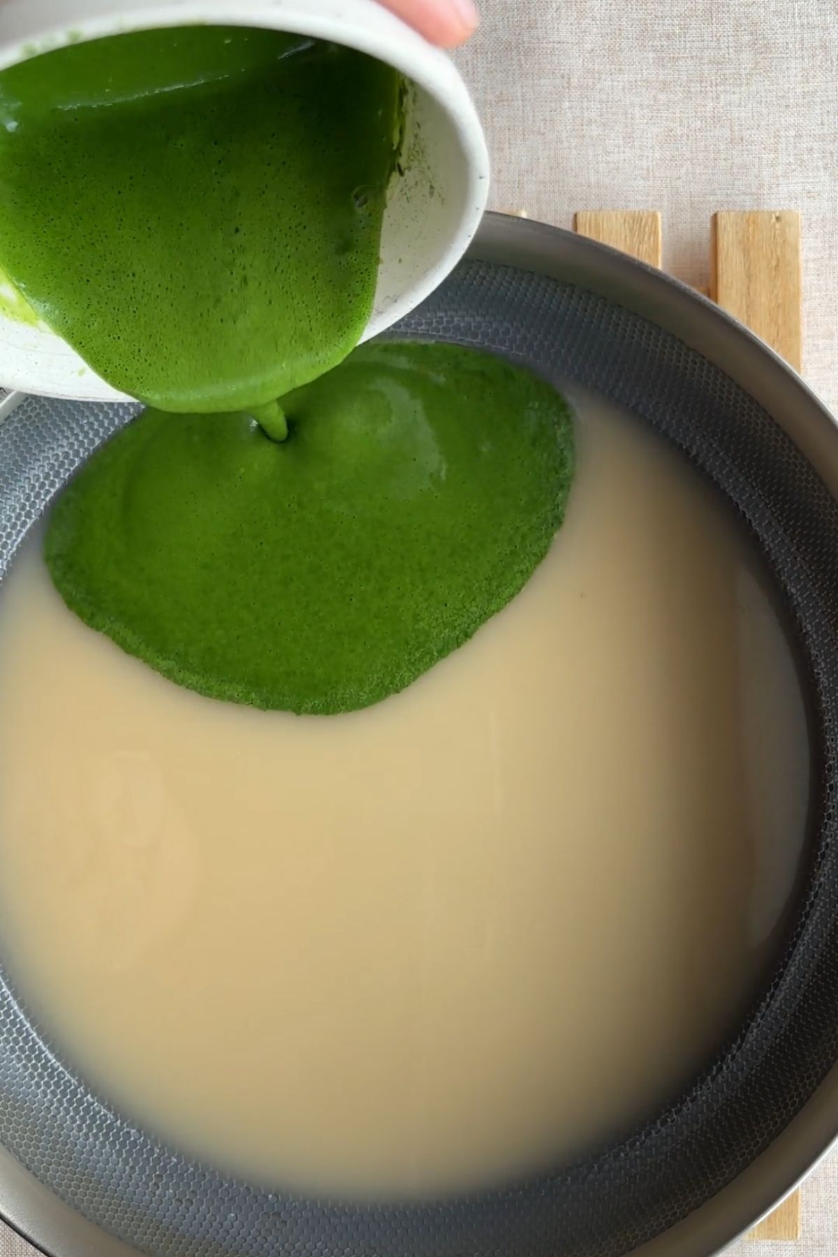 Bright green matcha mixture heating gently in a shallow pan.