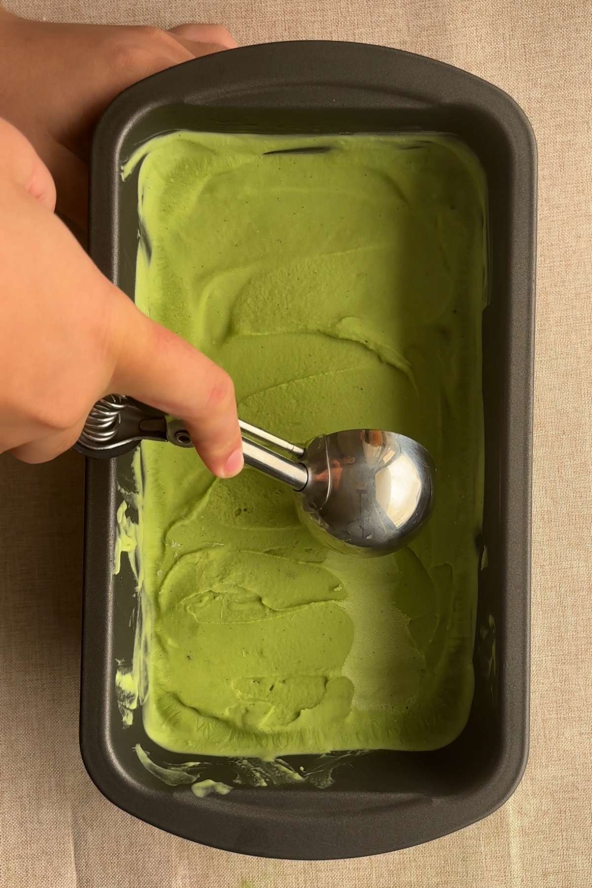 Ice cream scoop pressing into smooth green ice cream in a loaf pan.