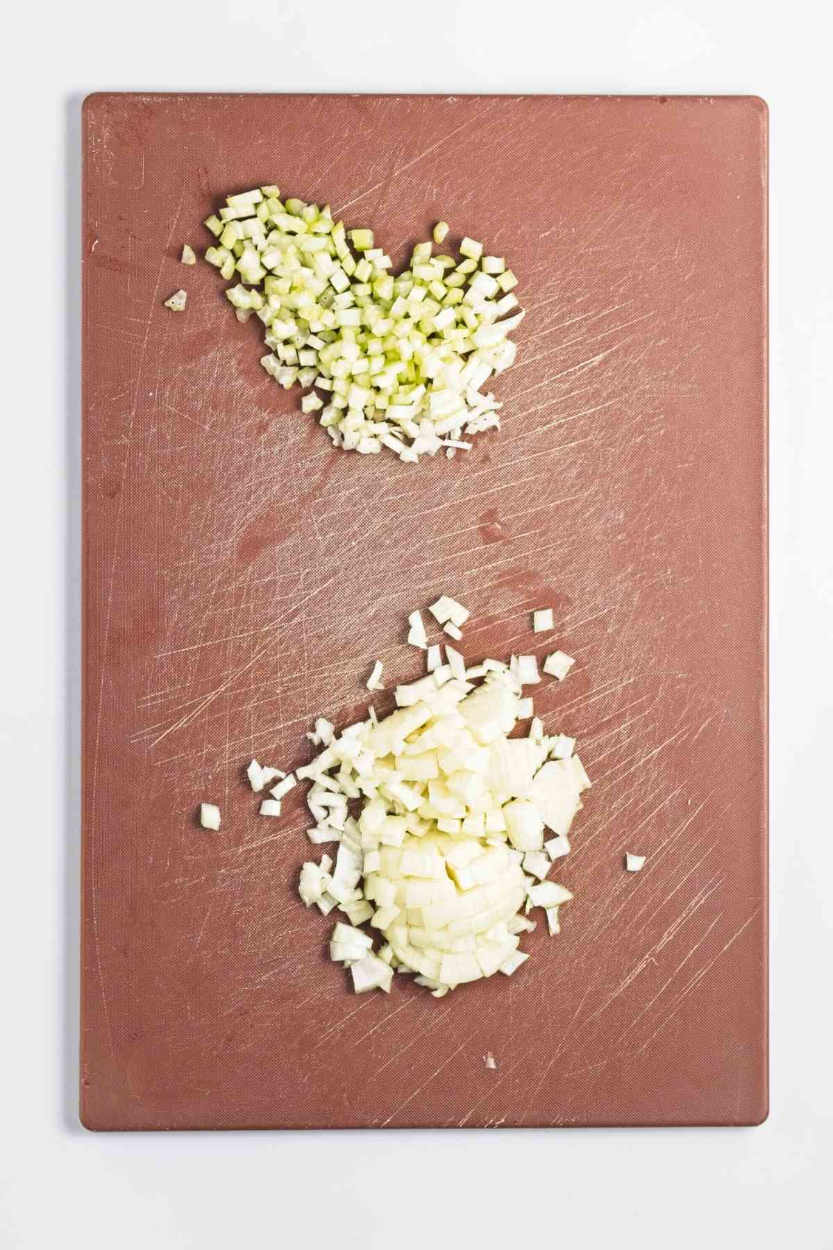 Finely diced onion and celery on a cutting board, prepped for cooking.