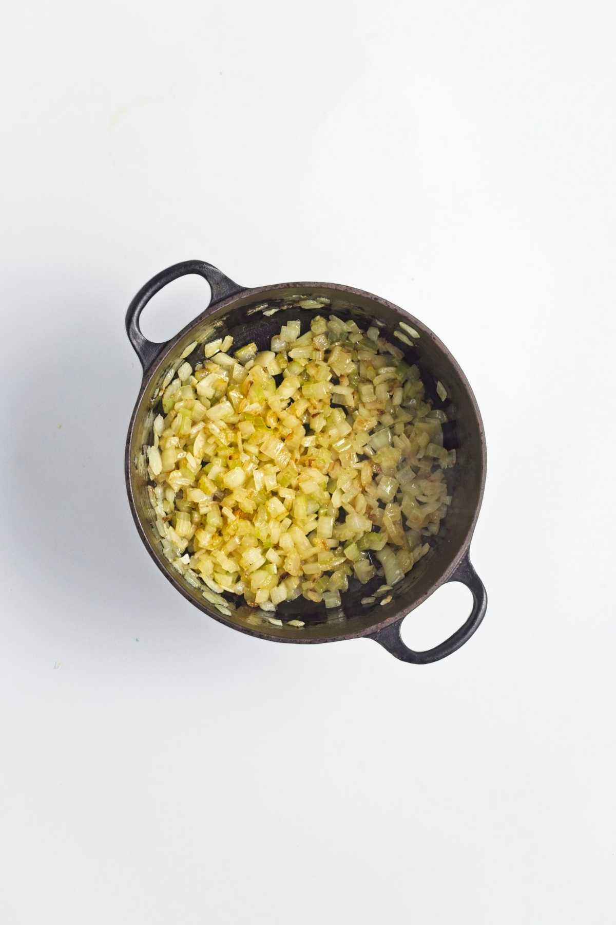 Diced onion and celery sautรฉing in a pot until softened and lightly golden.
