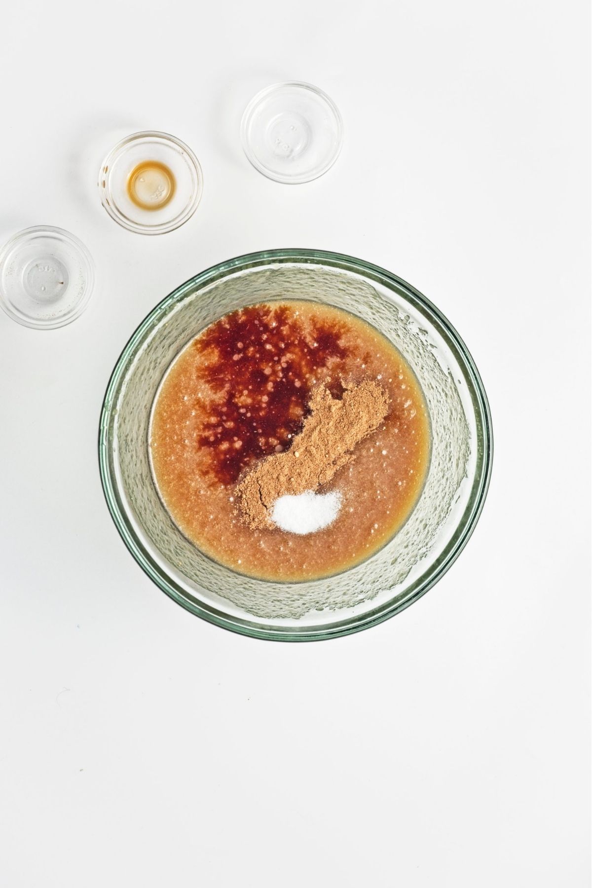 Oil, brown sugar, applesauce, vanilla, spices, and salt mixed together in a glass bowl.