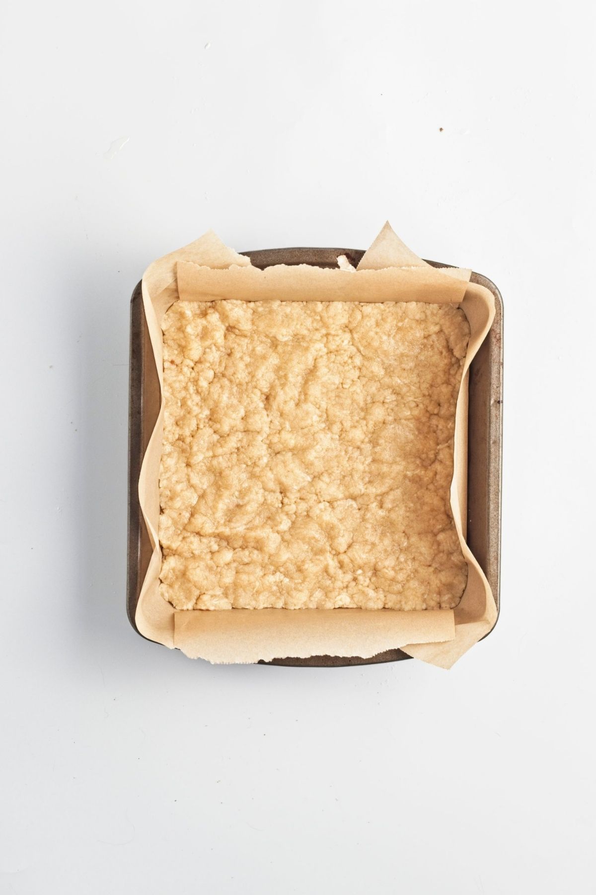 Crumbly dough pressed evenly into a parchment-lined square baking pan.