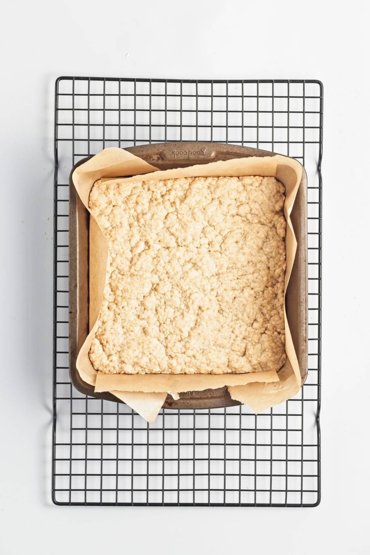Partially baked crust set and lightly golden in a parchment-lined pan on a cooling rack.
