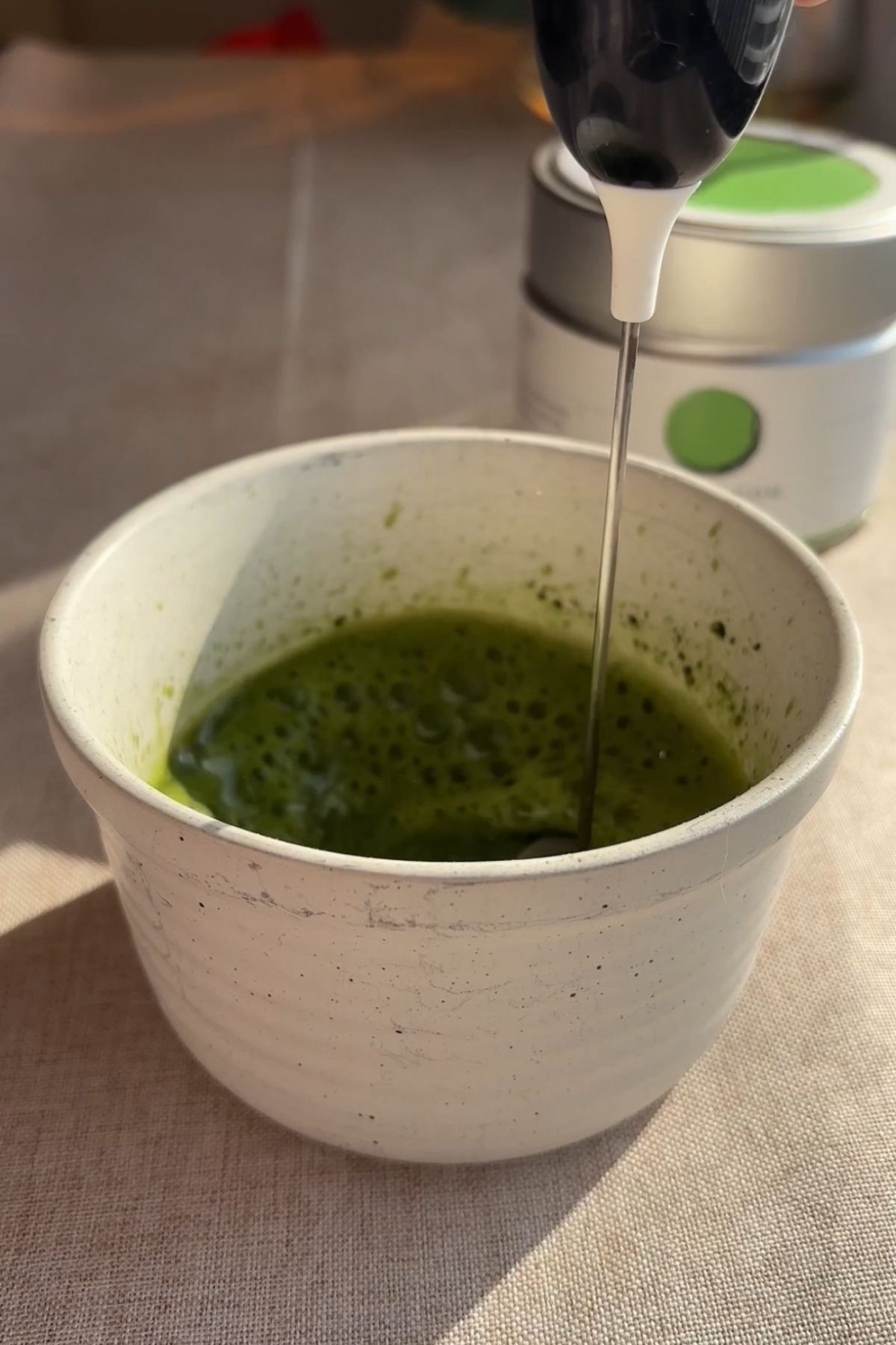 Handheld frother whisking matcha until smooth and foamy.