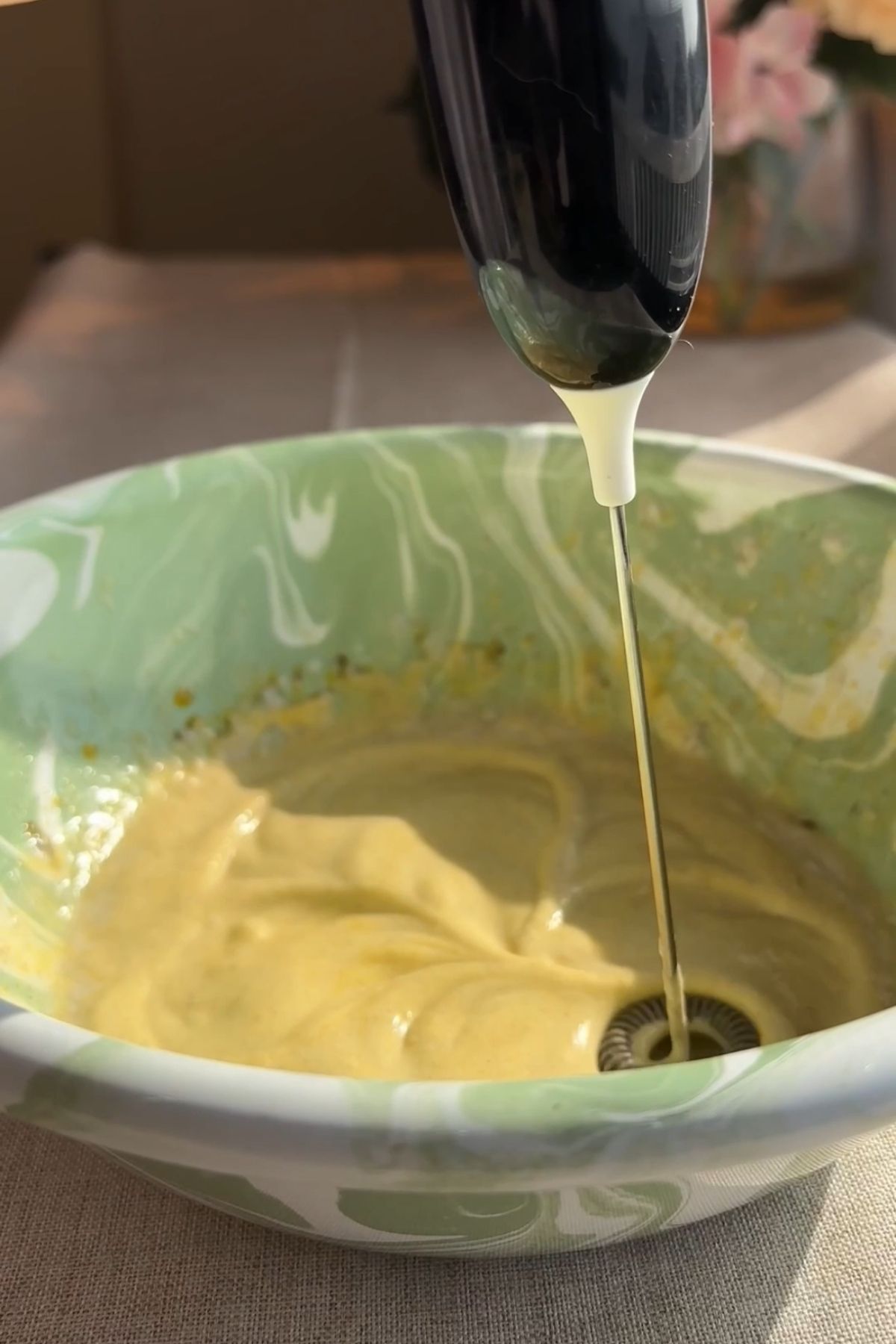 Handheld milk frother whisking pumpkin cold foam ingredients in a bowl.