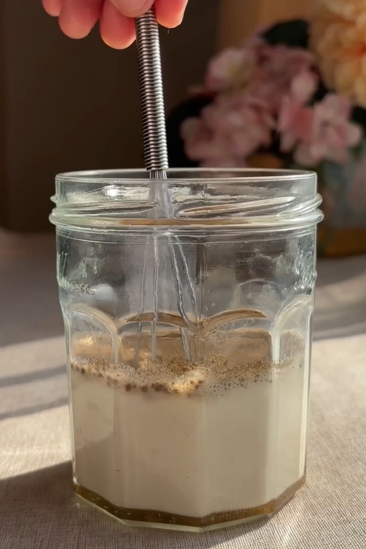 Milk and pumpkin spice being whisked together in a glass jar with a handheld frother.