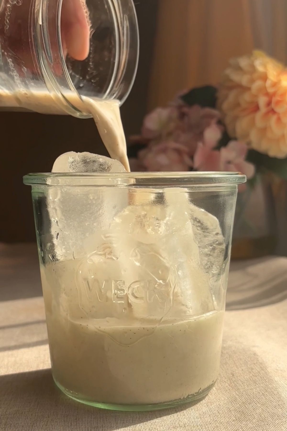 Spiced milk being poured from a small jar into a glass filled with ice.