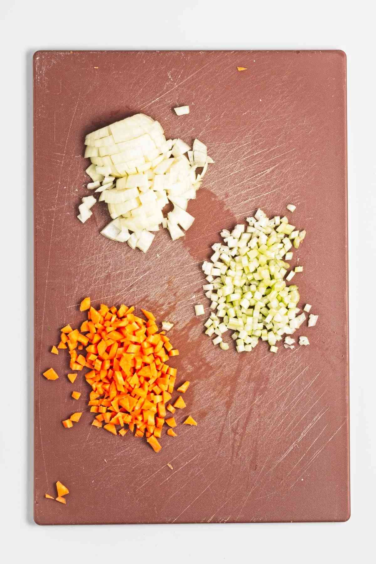 Diced onion, carrot, and celery arranged separately on a cutting board.