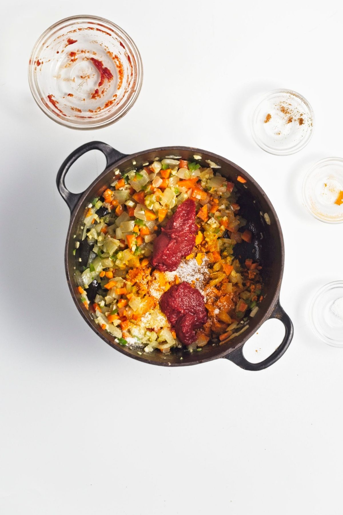 Spices and tomato paste added to sautรฉed vegetables in a pot.