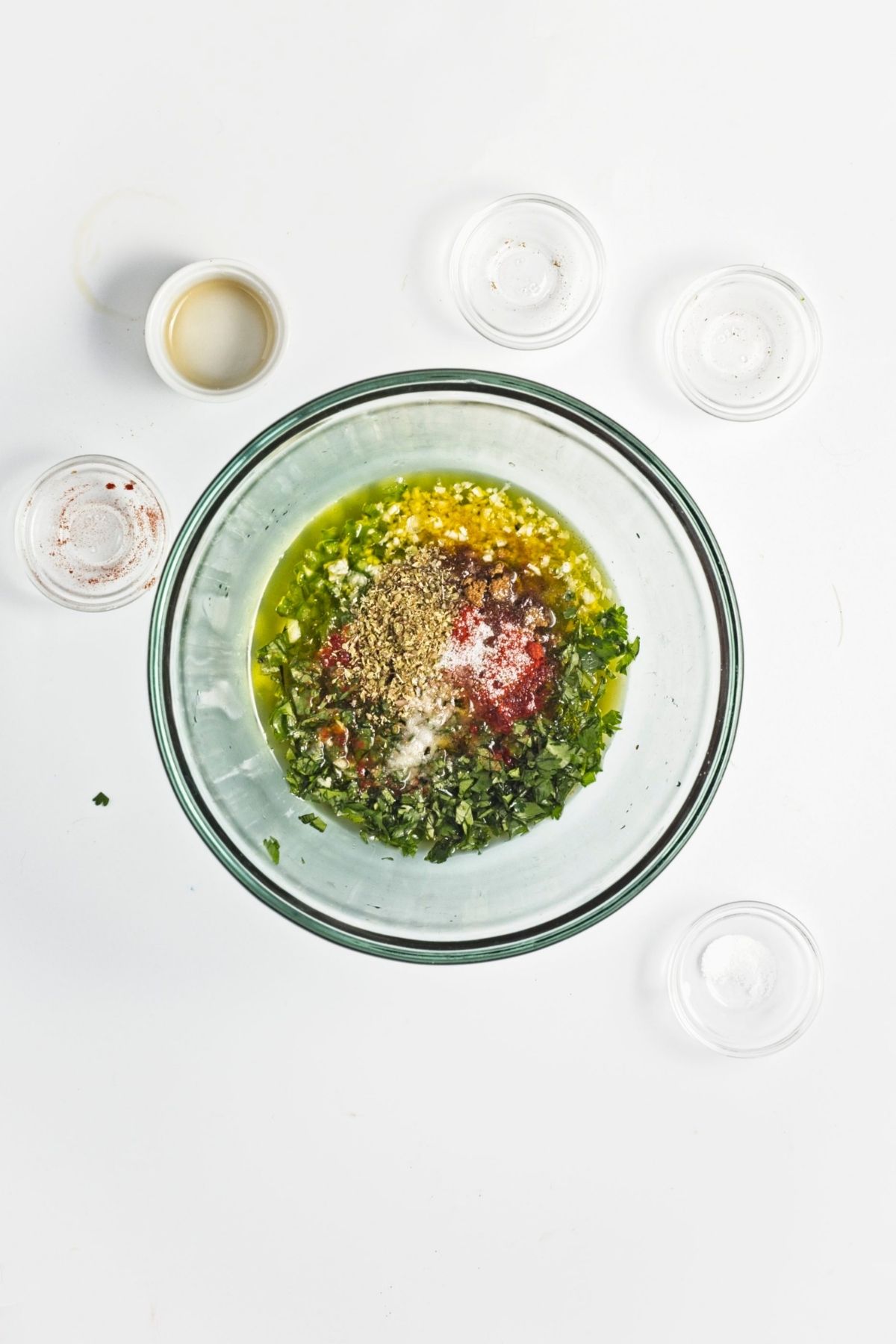 Olive oil, herbs, spices, garlic, and lime juice combined in a glass bowl for dressing.