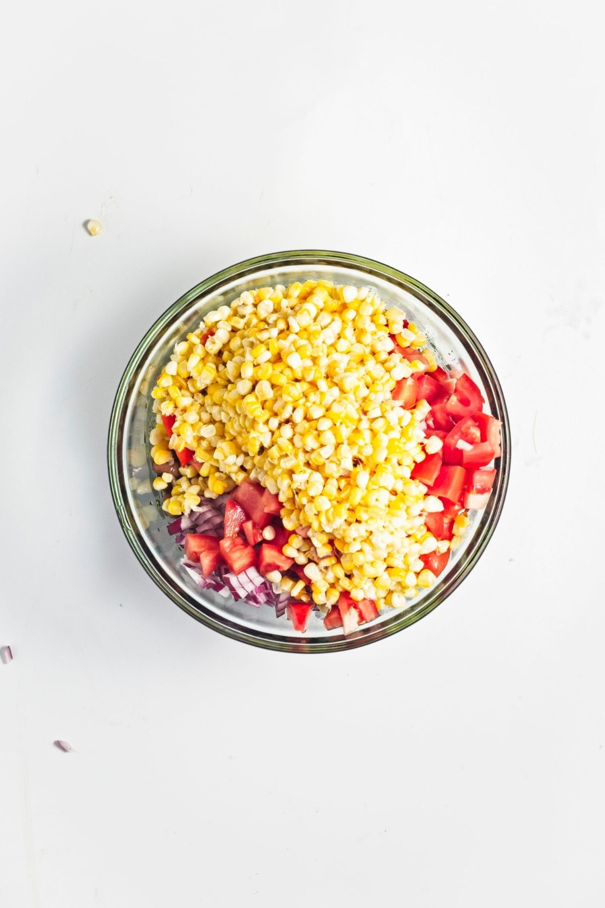 Chopped corn, tomatoes, and red onion added to a glass mixing bowl.